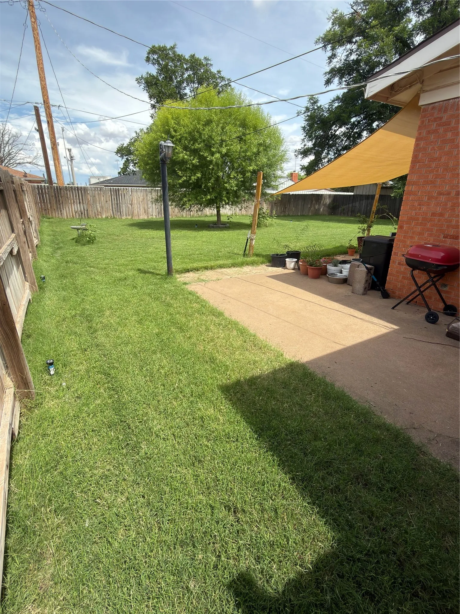 Expansive backyard featuring a large green lawn, mature trees, a concrete patio area, and perimeter fencing