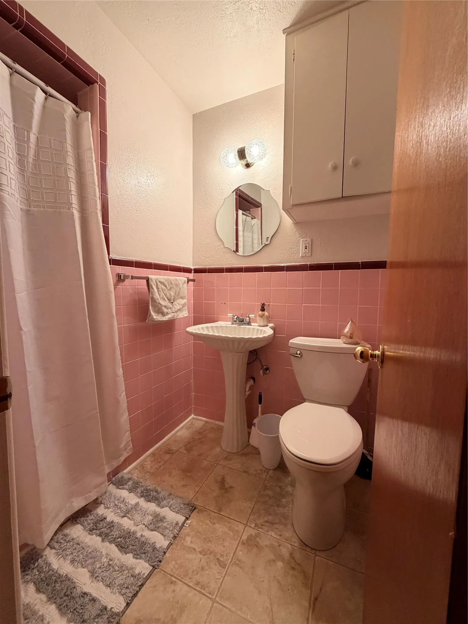 Bathroom featuring pink wall tiling, pedestal sink, and tiled flooring