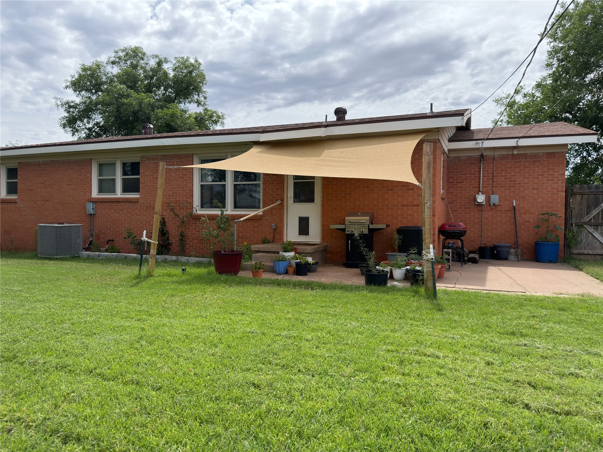 Expansive rear yard featuring a red brick exterior, a paved patio, a sun shade, and a green lawn