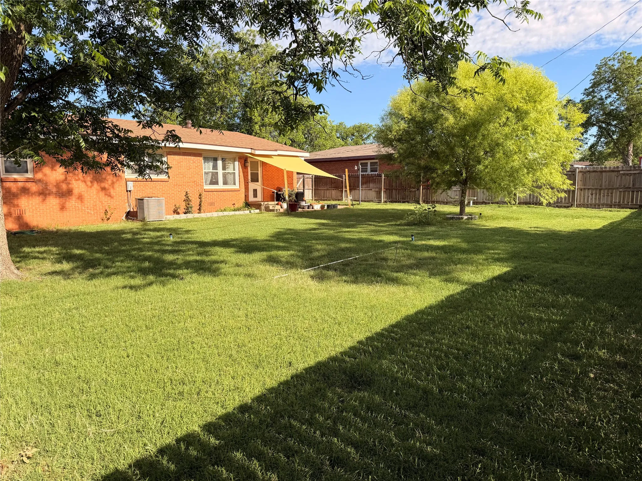 Expansive backyard featuring a manicured lawn, mature trees, and a wooden privacy fence