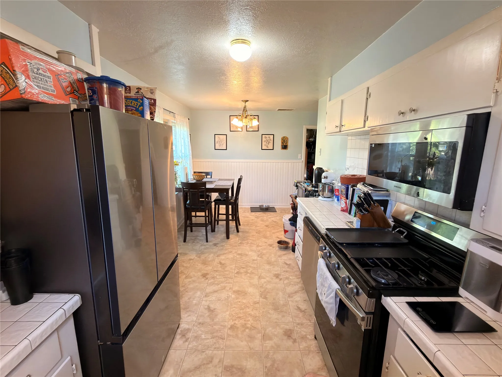 Kitchen featuring a gas range, stainless steel microwave, white cabinetry, tile countertops, and vinyl flooring