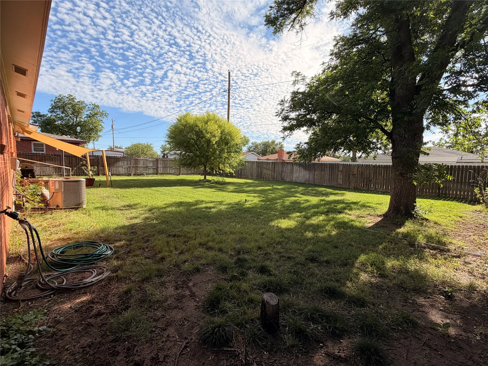 Spacious backyard featuring a substantial grassy area, mature trees, and a full privacy fence