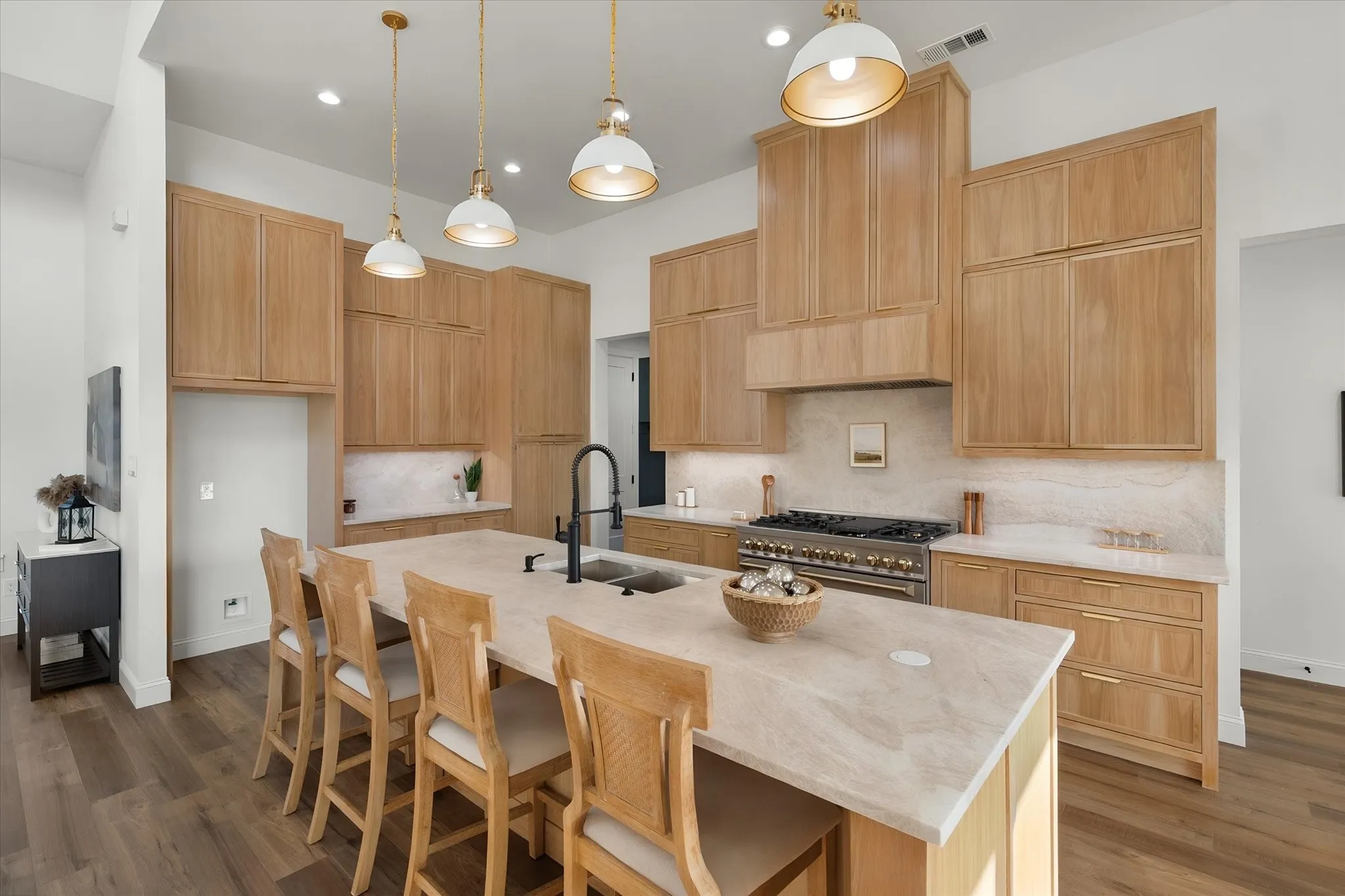 Statement pendant lighting complements the oversized island and natural wood kitchen cabinetry.