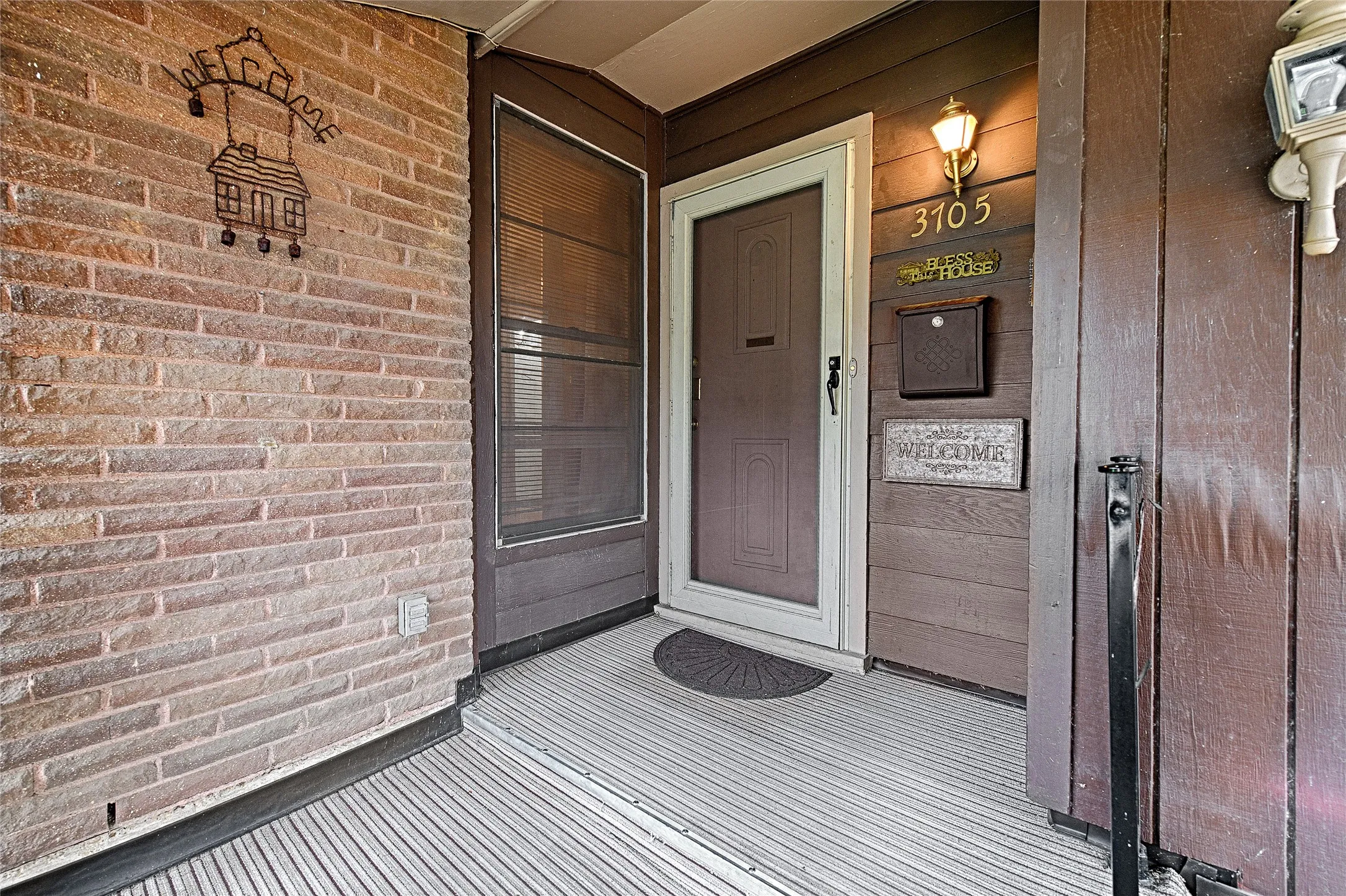 Inviting front porch featuring a brick facade, wood-finish siding, and a screen door