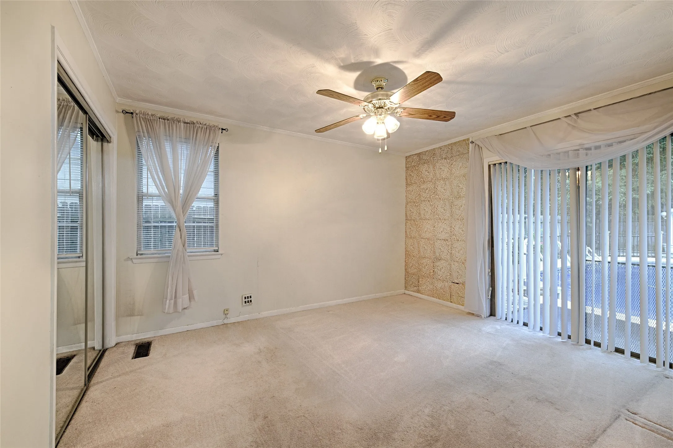Carpeted room featuring a ceiling fan with light fixture, sliding mirrored closet doors, a window with blinds, and a sliding glass door