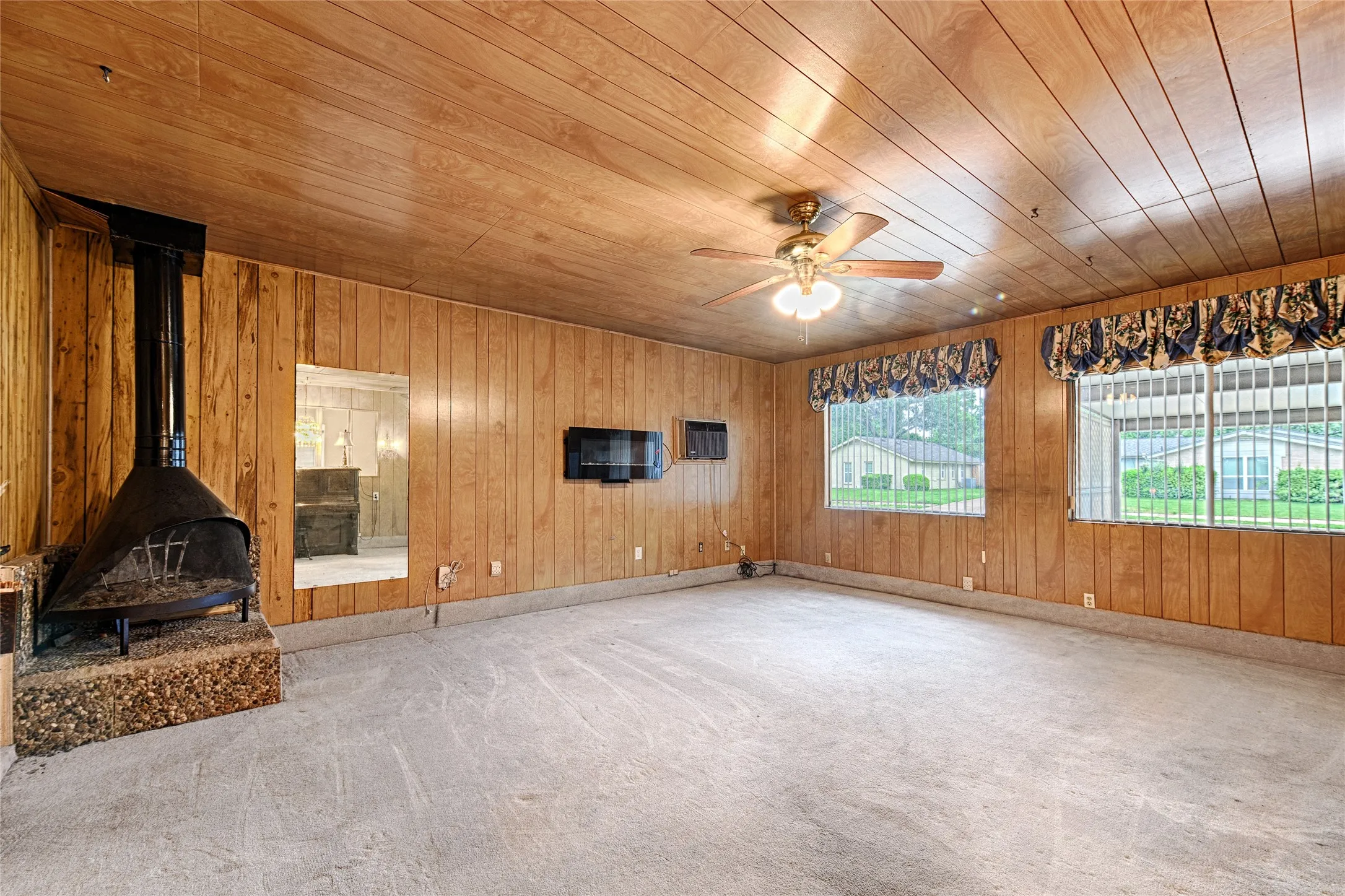 Spacious interior room featuring wood-panel walls, a freestanding fireplace with a stone-finish hearth, and a ceiling fan