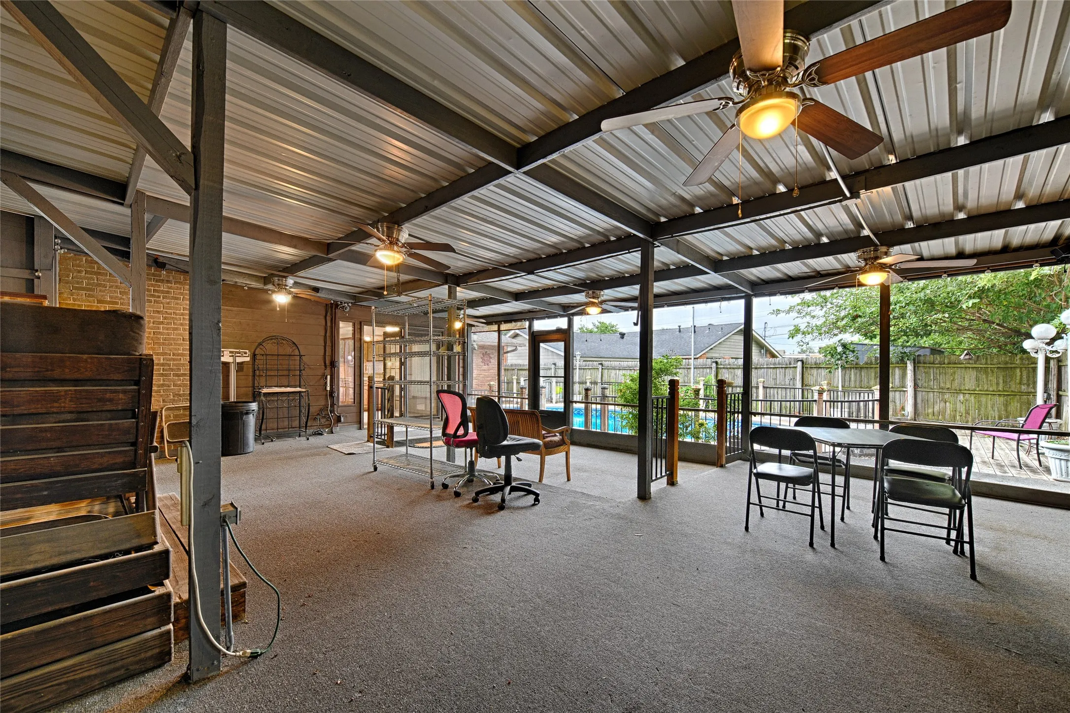Expansive covered patio featuring a corrugated metal roof, multiple ceiling fans with integrated lighting, and a brick exterior wall