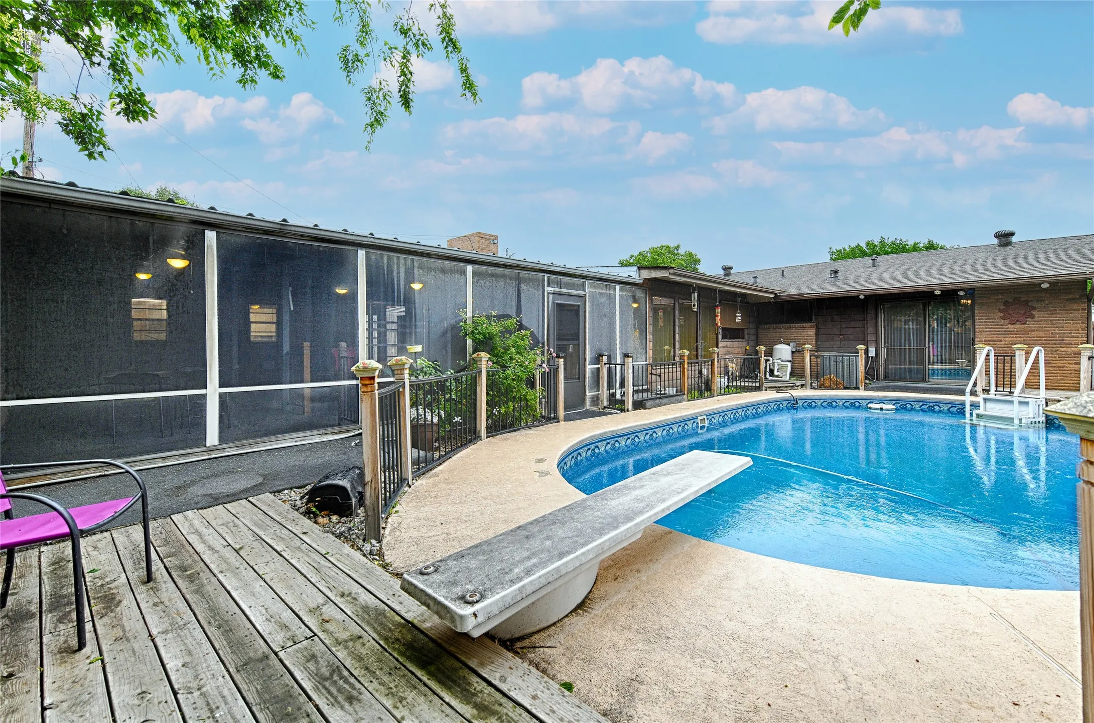Outdoor swimming pool with integrated diving board, surrounded by concrete decking and a wood deck area