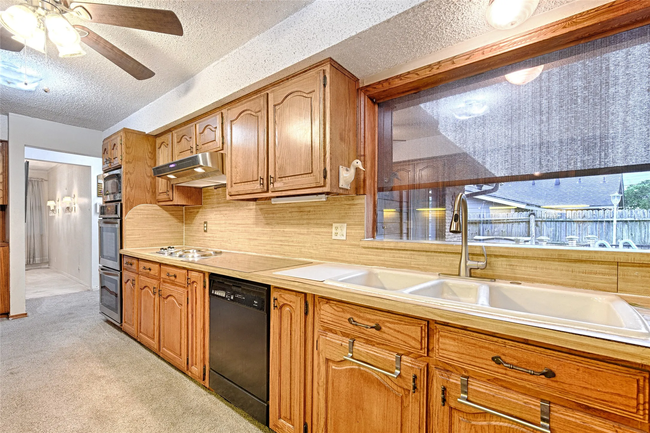 Kitchen featuring wood cabinetry with decorative hardware, a double basin sink, a built-in oven and microwave unit, a cooktop, and a stainless steel range hood