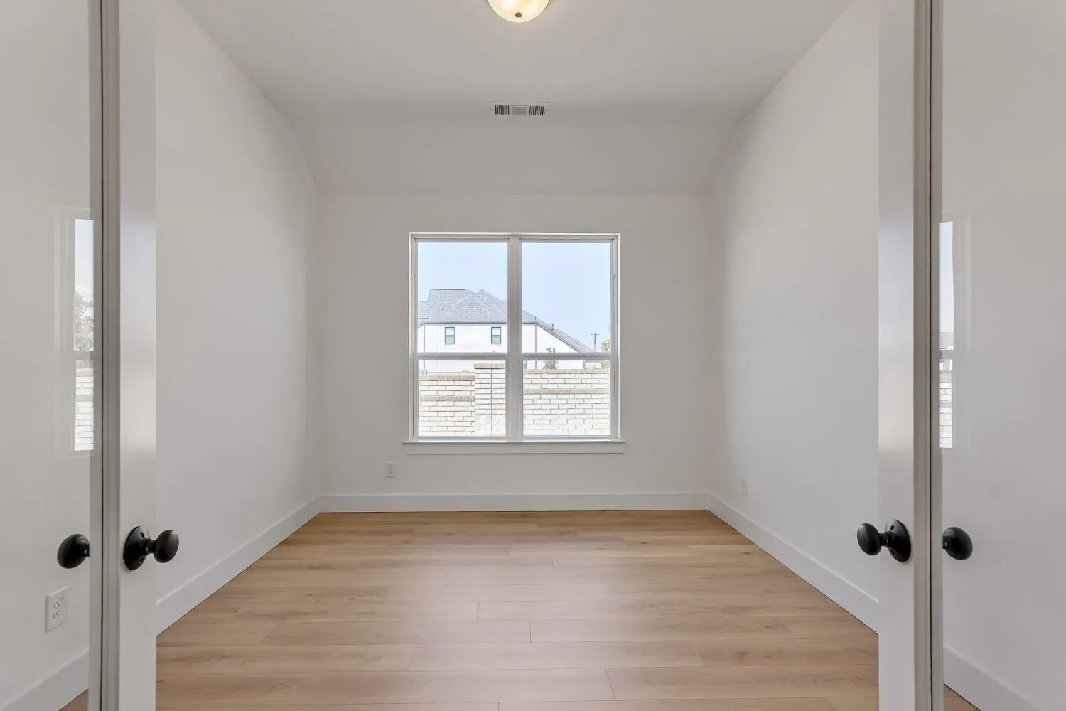 Room featuring wood-finish flooring, white baseboards, a central window, and white walls