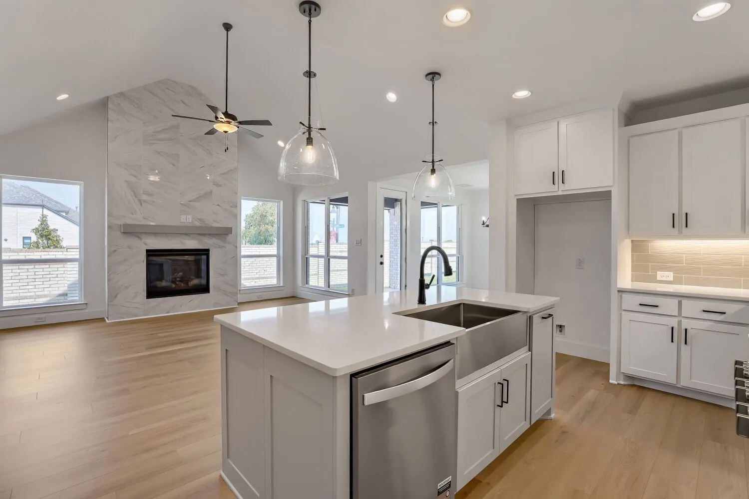 Open-concept kitchen featuring a center island with a farmhouse sink, light cabinetry with dark hardware, a subway tile backsplash, and stainless steel appliances