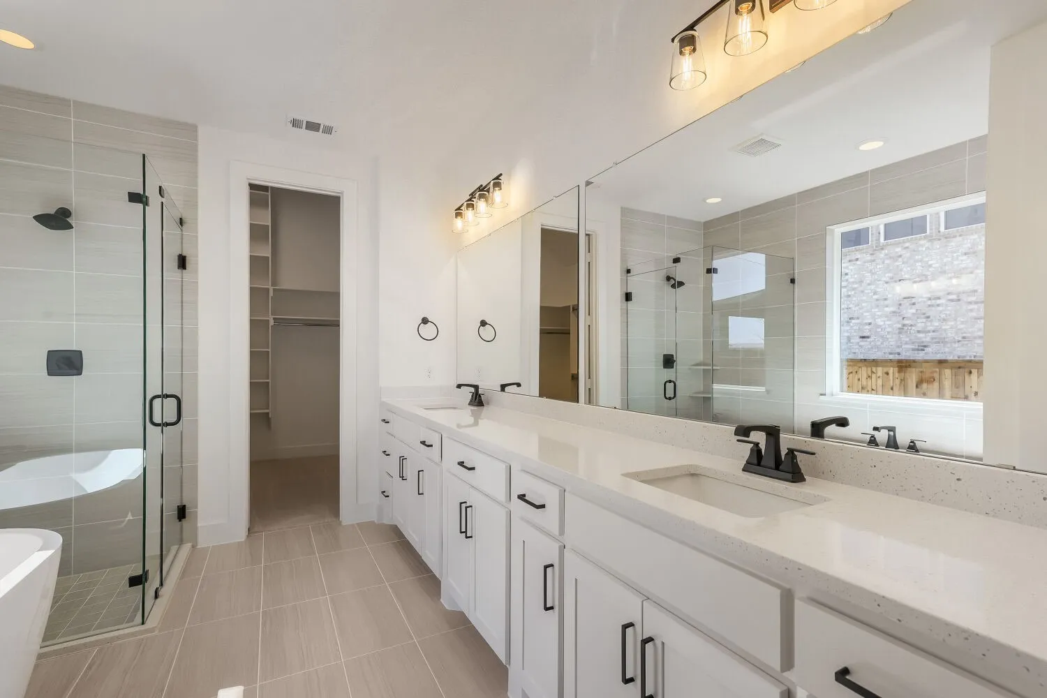 Bathroom vanity featuring dual sinks with matte black fixtures, an expansive mirror, and a three-light fixture