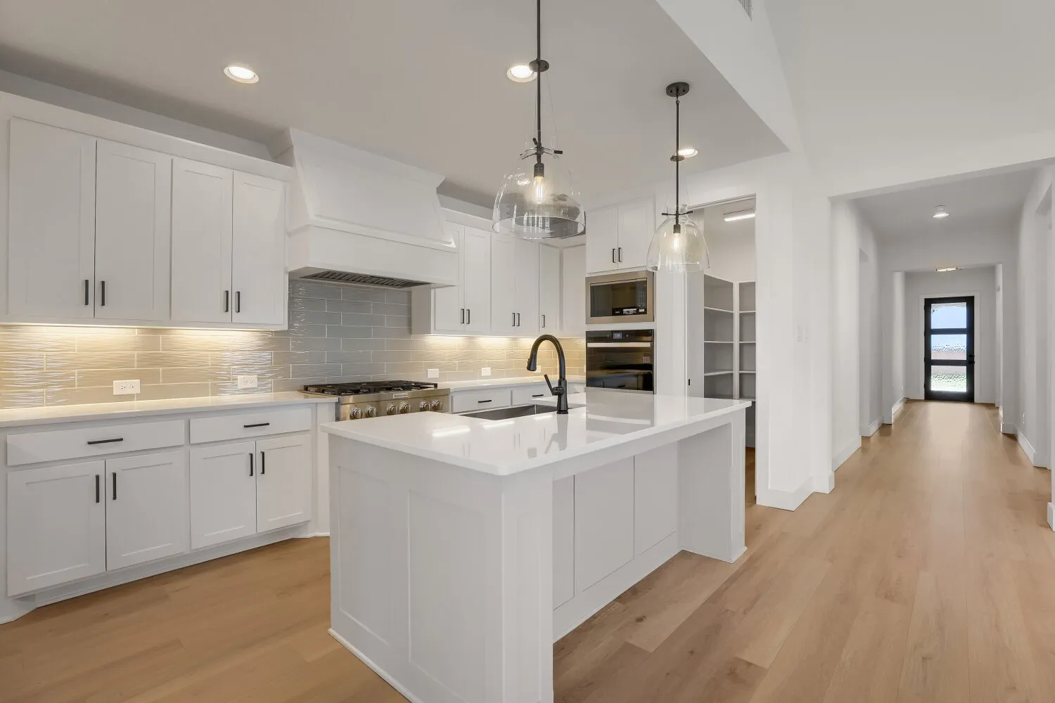 Modern kitchen featuring white shaker cabinetry, an expansive center island with a sink, stainless steel appliances, and a light-toned wood-finish flooring