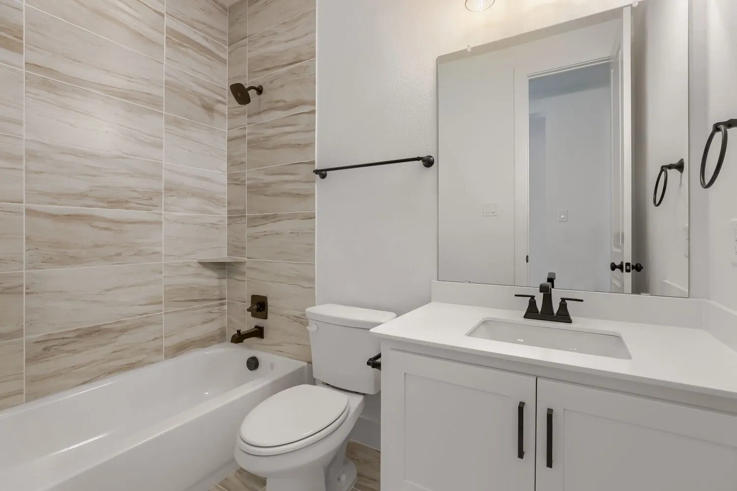 Bathroom featuring a white vanity with an integrated sink, matte black fixtures, and a tiled shower surround with a built-in niche