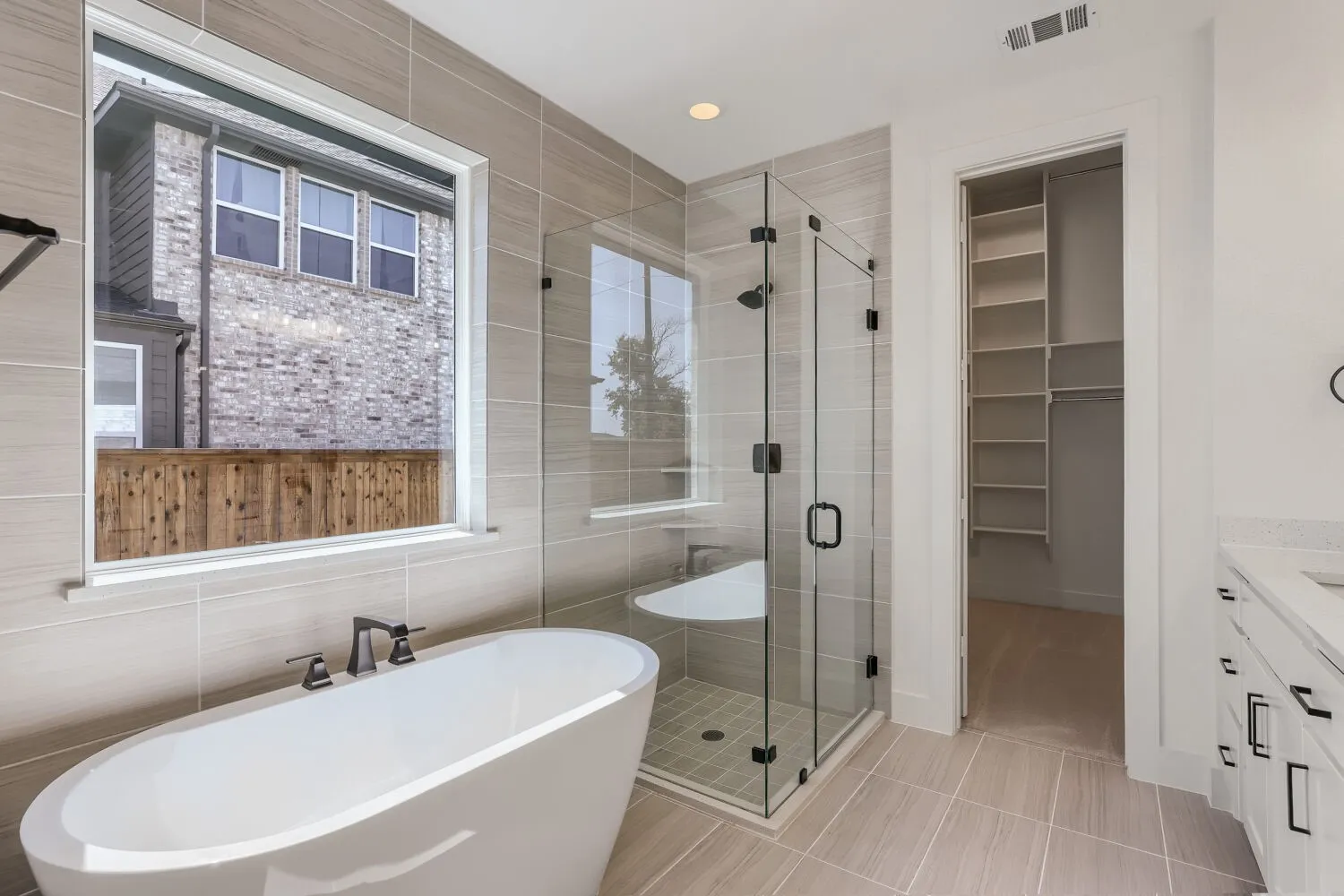 Contemporary bathroom with a freestanding soaking tub, a glass-enclosed shower with a built-in bench, and light-toned tile flooring