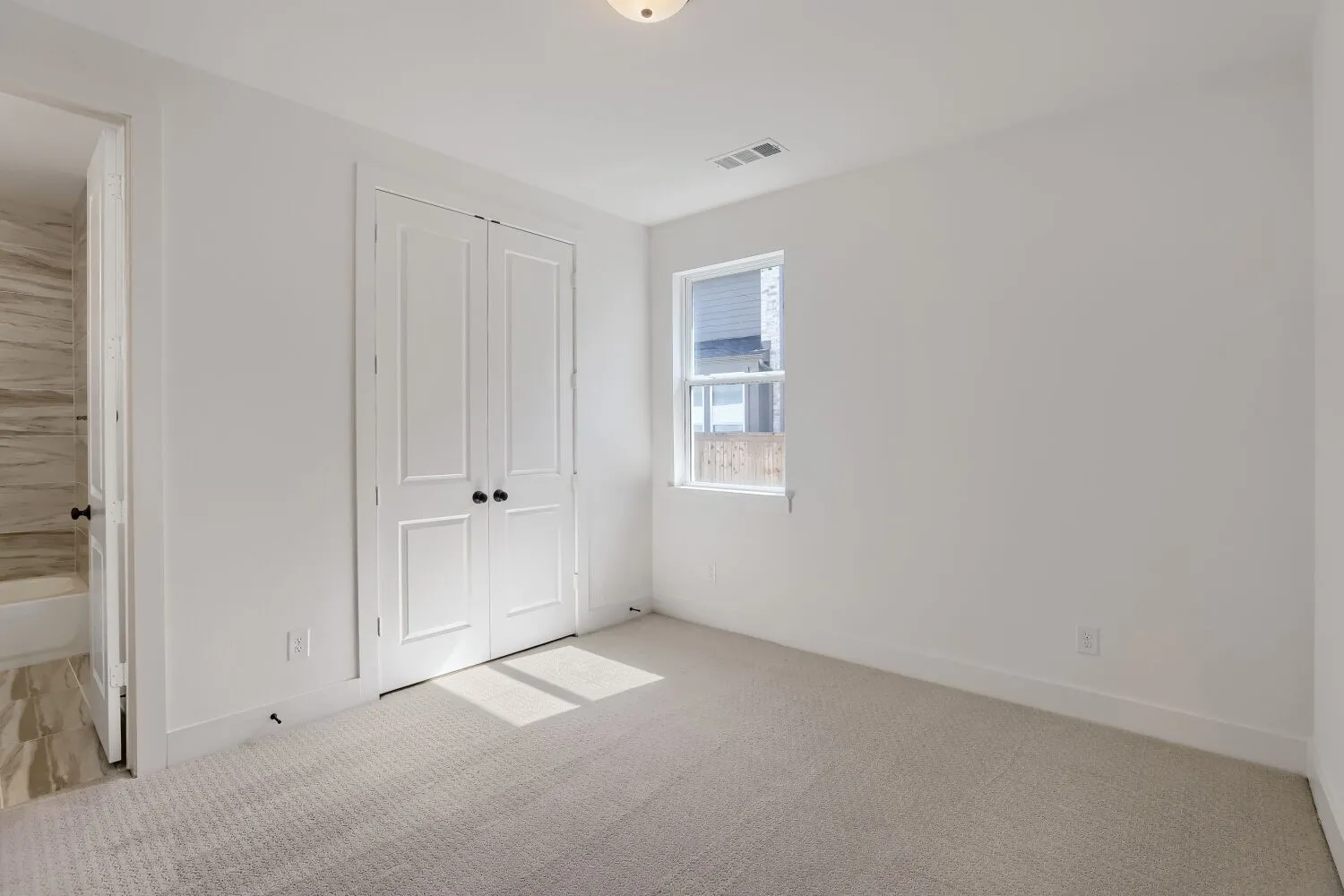 Neutral carpeted room with white walls, a single window, and double panel doors