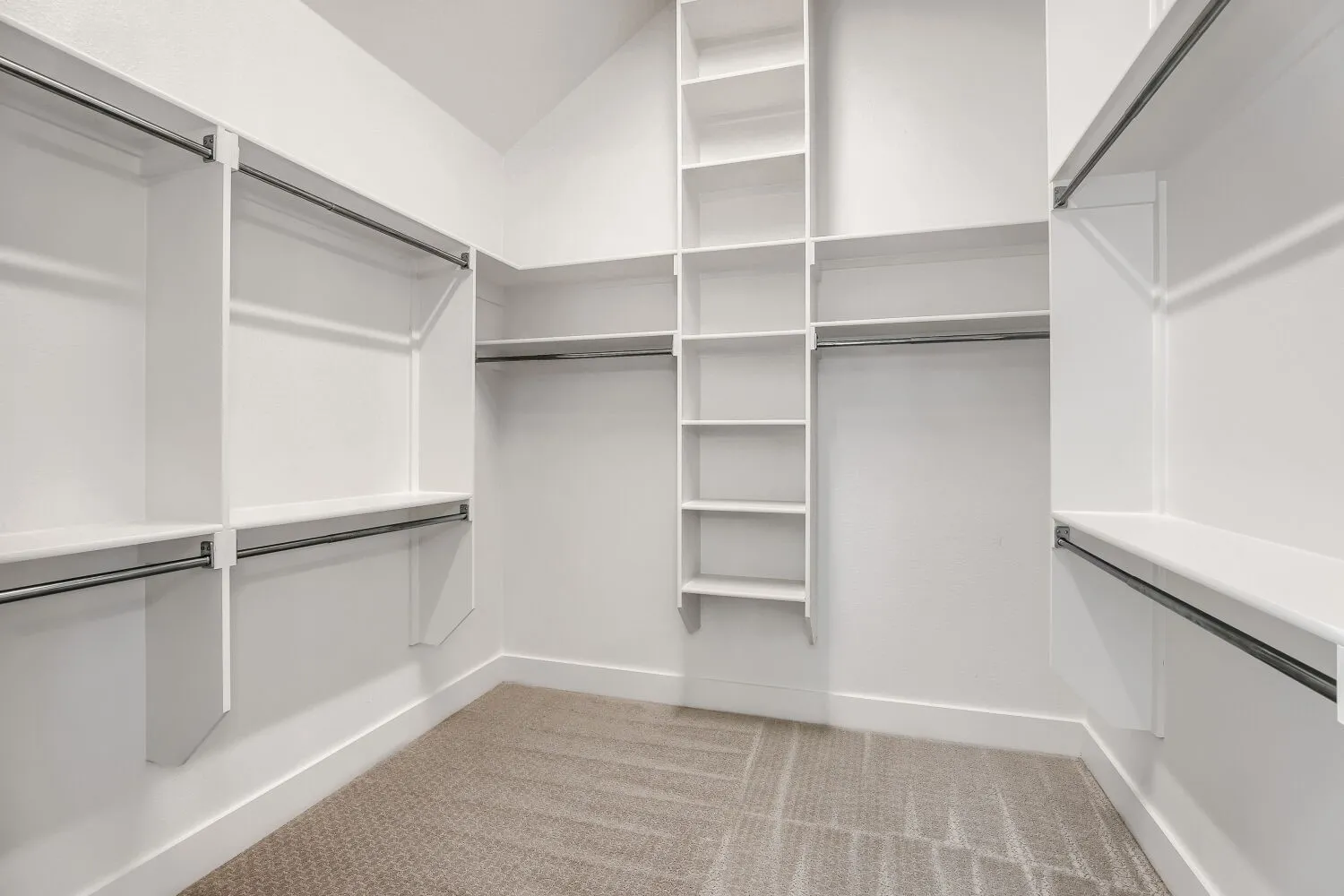 Walk-in closet featuring white built-in shelving, multiple hanging rods, and light-toned carpet flooring