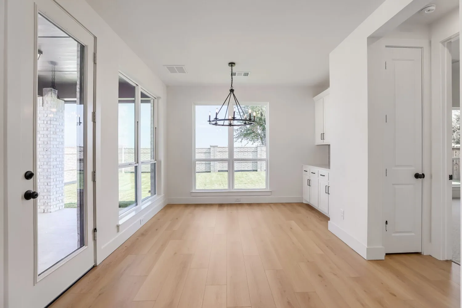 Open-concept interior featuring light wood-finish flooring, white walls, and a modern black chandelier
