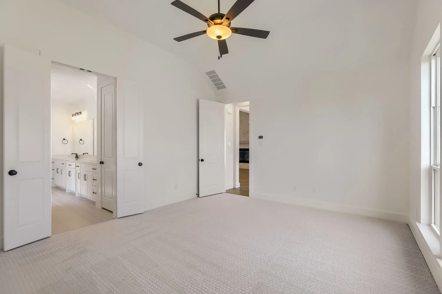Carpeted interior space featuring a vaulted ceiling with a ceiling fan, a window, and two doorways