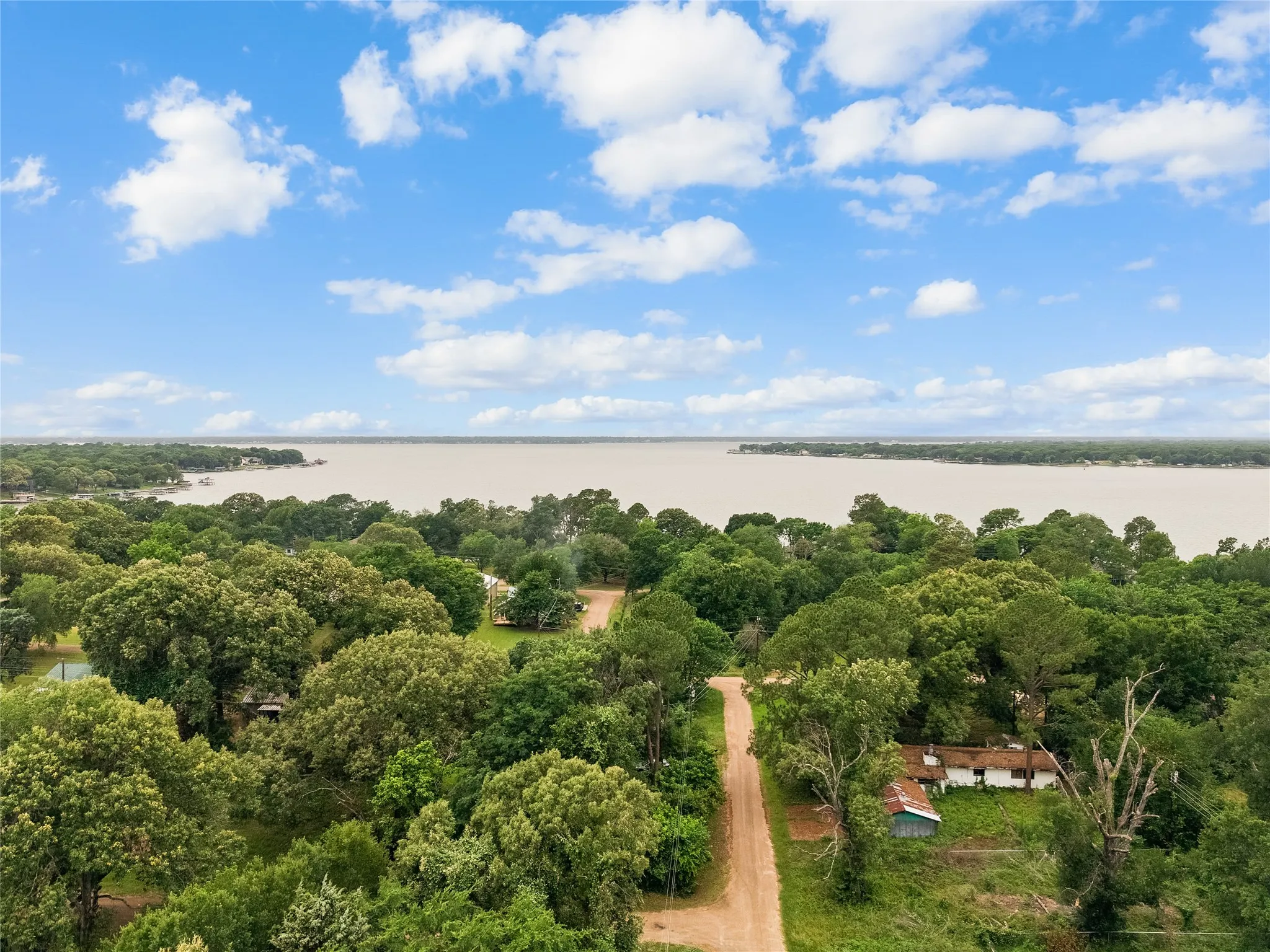 Expansive waterfront setting featuring a wide body of water, lush green tree canopy, and a partially visible residential structure