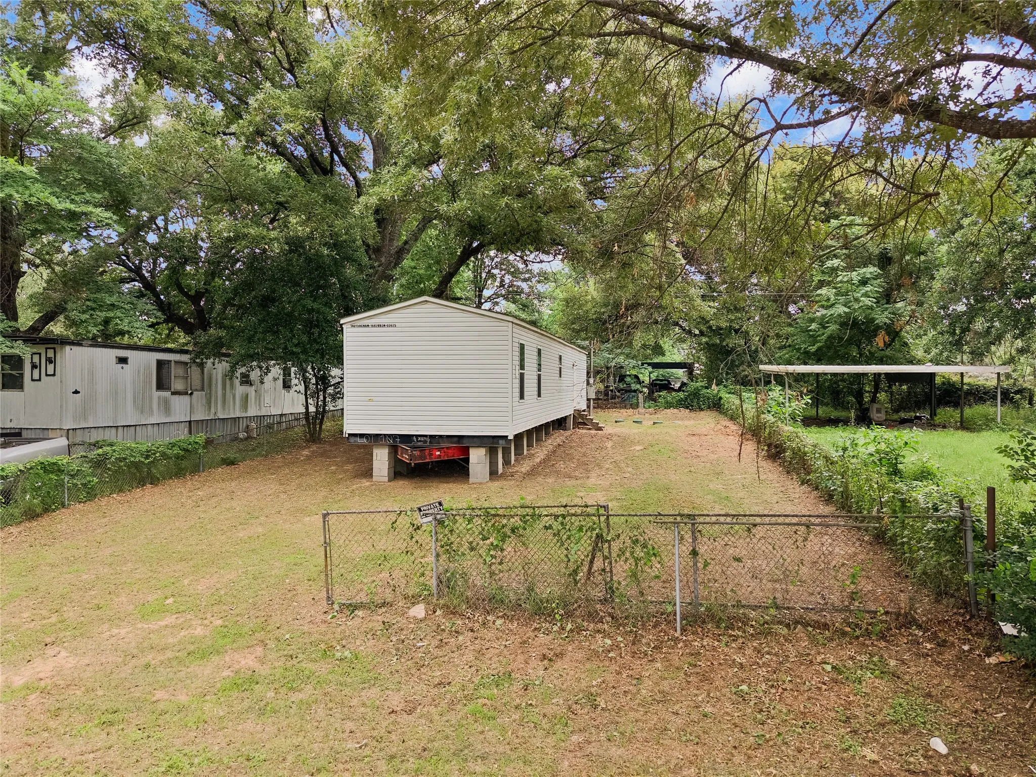 Expansive lot featuring a single-wide manufactured home with white siding, elevated on concrete block supports