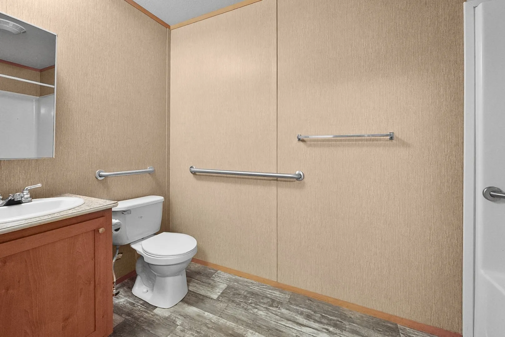 Bathroom featuring a wood-finish vanity with a built-in sink, a standard toilet, and wood-finish flooring