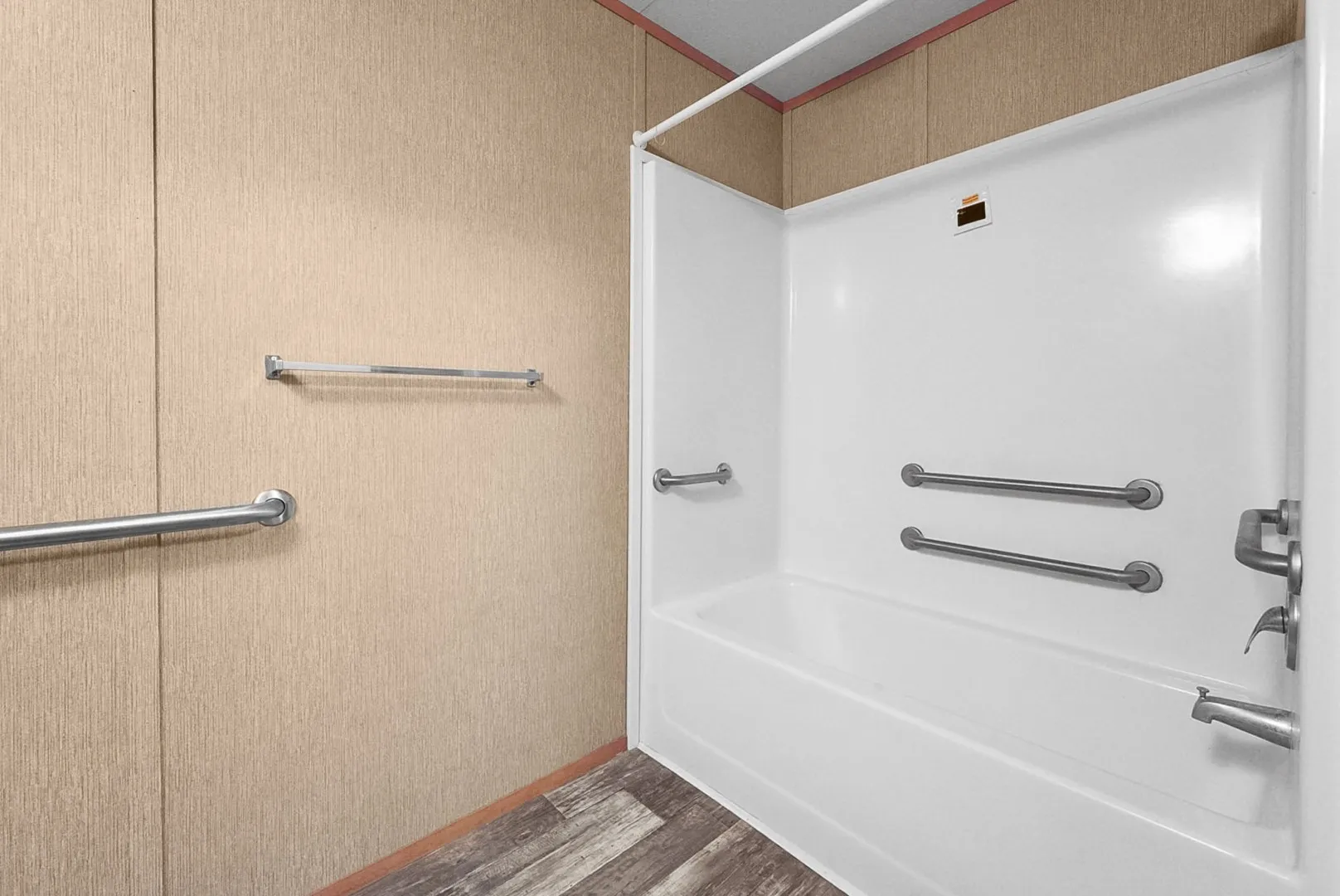 Bathtub and shower combination with white surround, integrated grab bars, chrome fixtures, and wood-finish flooring