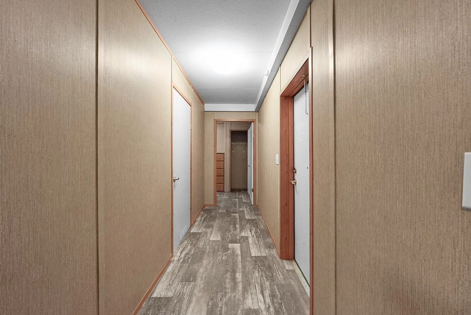 Hallway featuring wood-finish paneling, wood-finish flooring, white doors, and overhead lighting