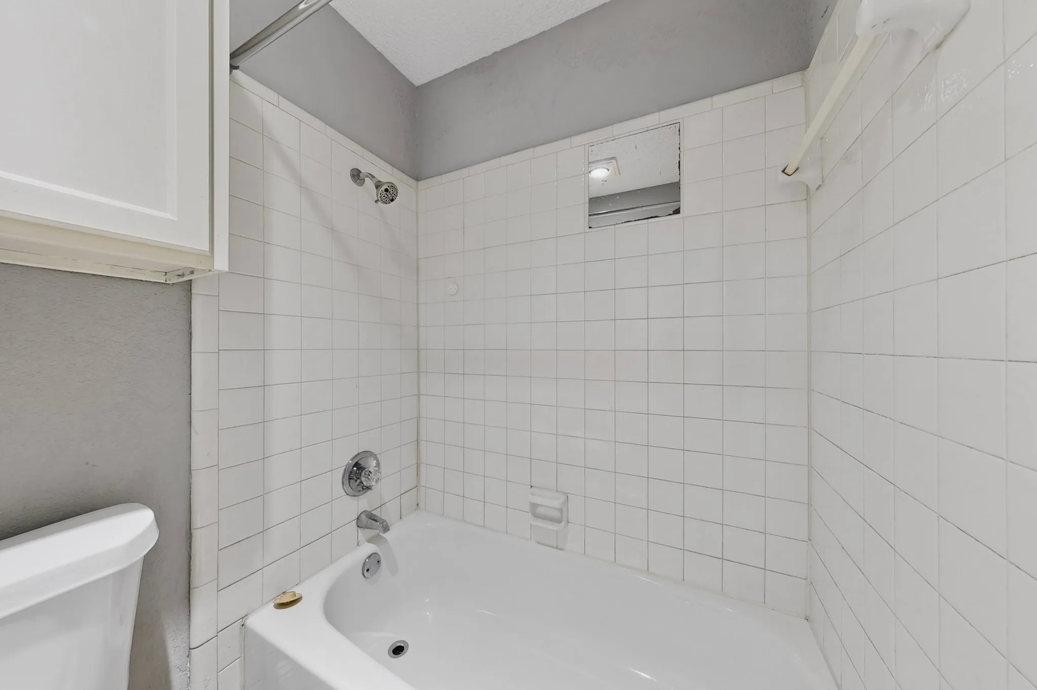 Bathtub with white tile surround, chrome fixtures, and a showerhead