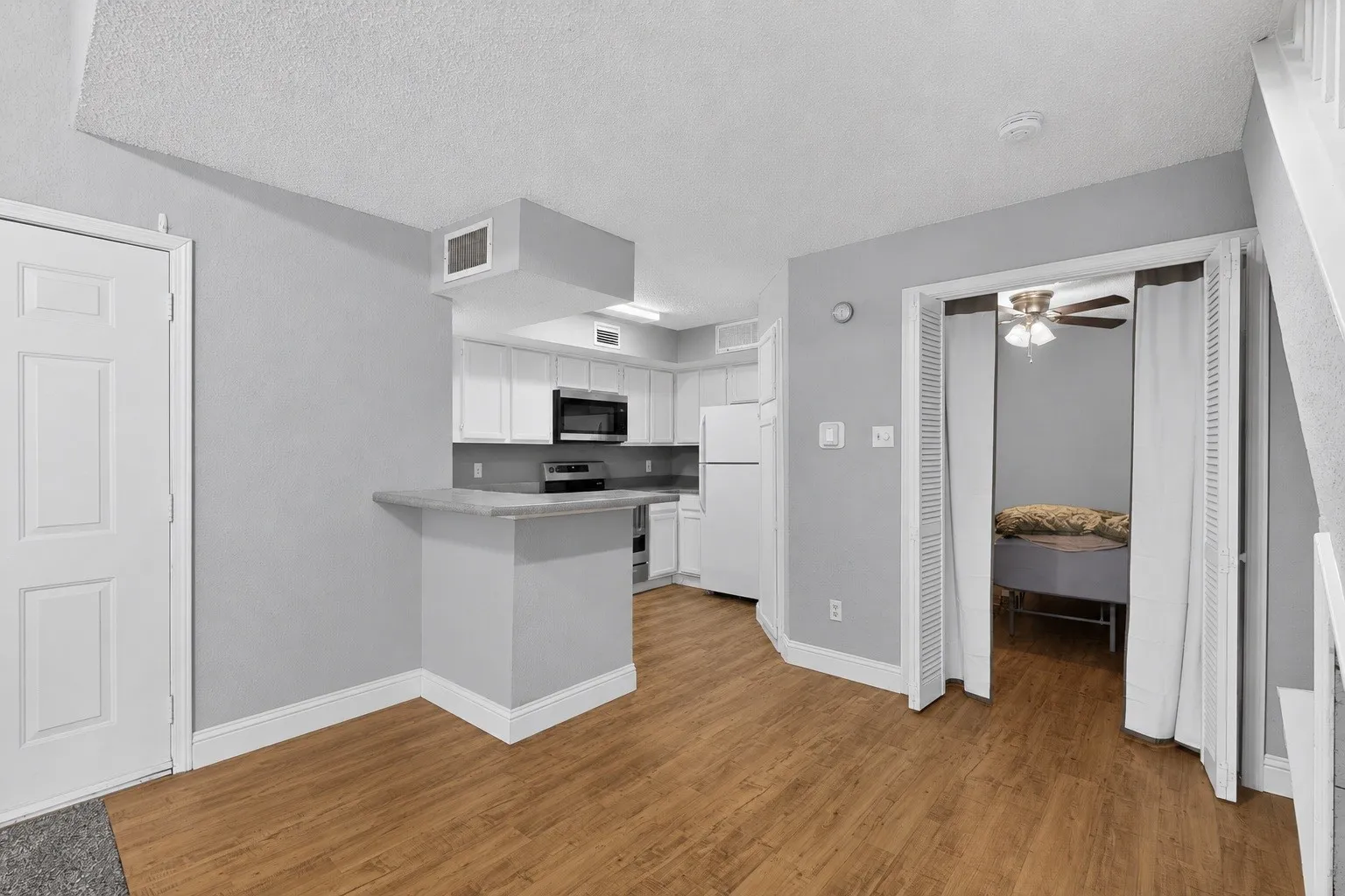 Open-concept living area featuring wood-finish flooring, a kitchen with white cabinetry and stainless steel appliances, a breakfast bar, light gray walls, and white trim throughout