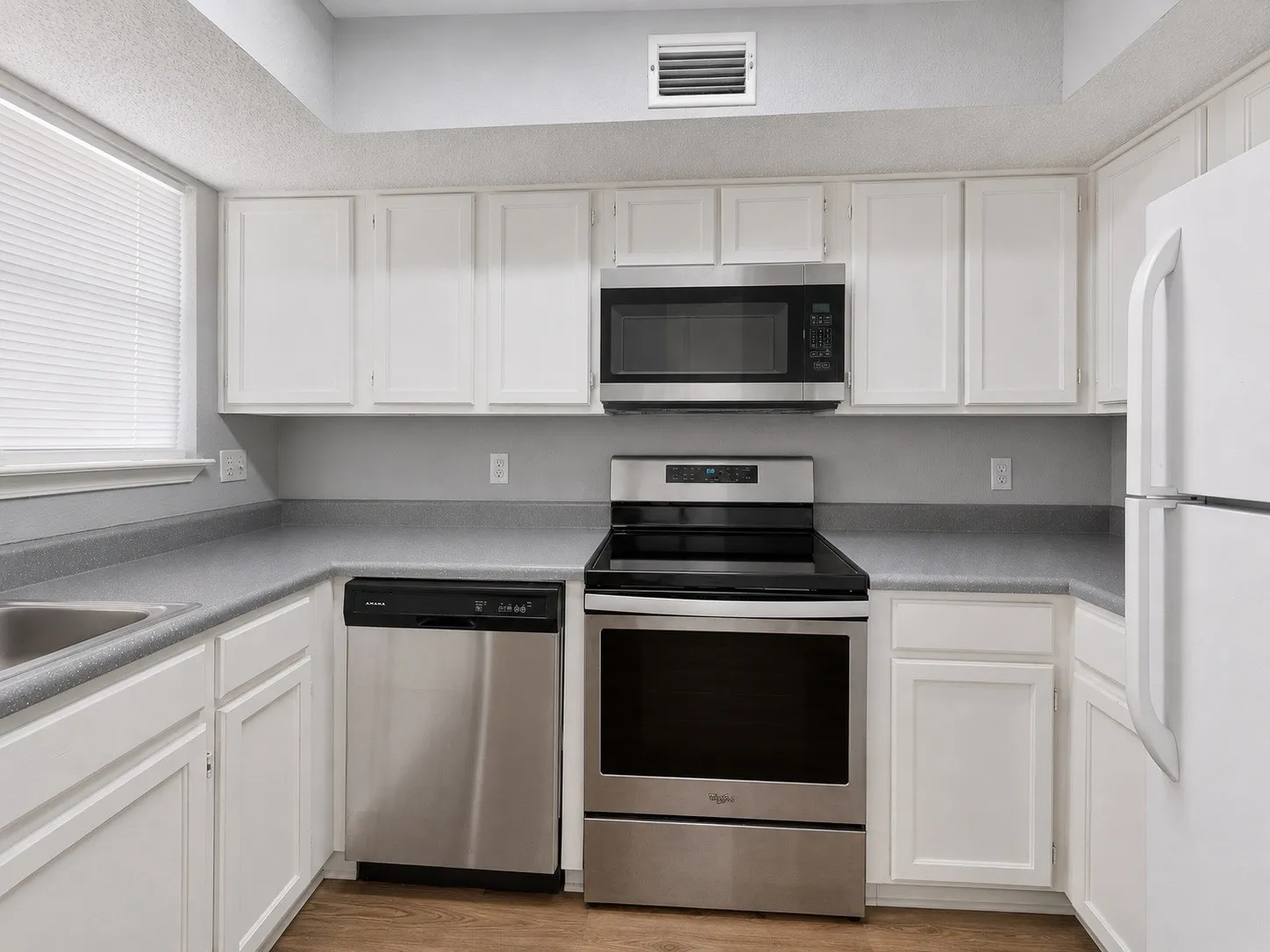 Kitchen featuring white cabinetry, grey countertops, stainless steel appliances, and a window with blinds
