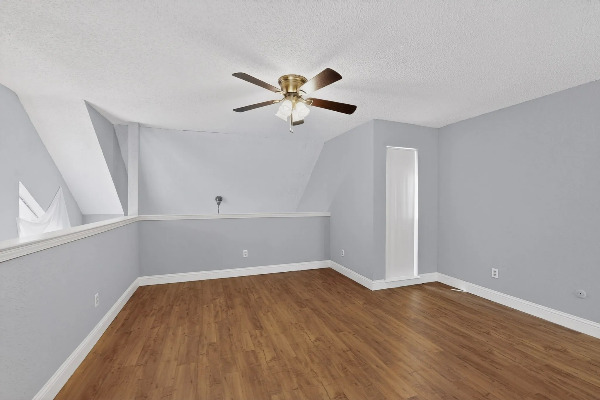 Spacious room featuring wood-finish flooring, light blue wall paint, a ceiling fan with integrated lighting, and white trim