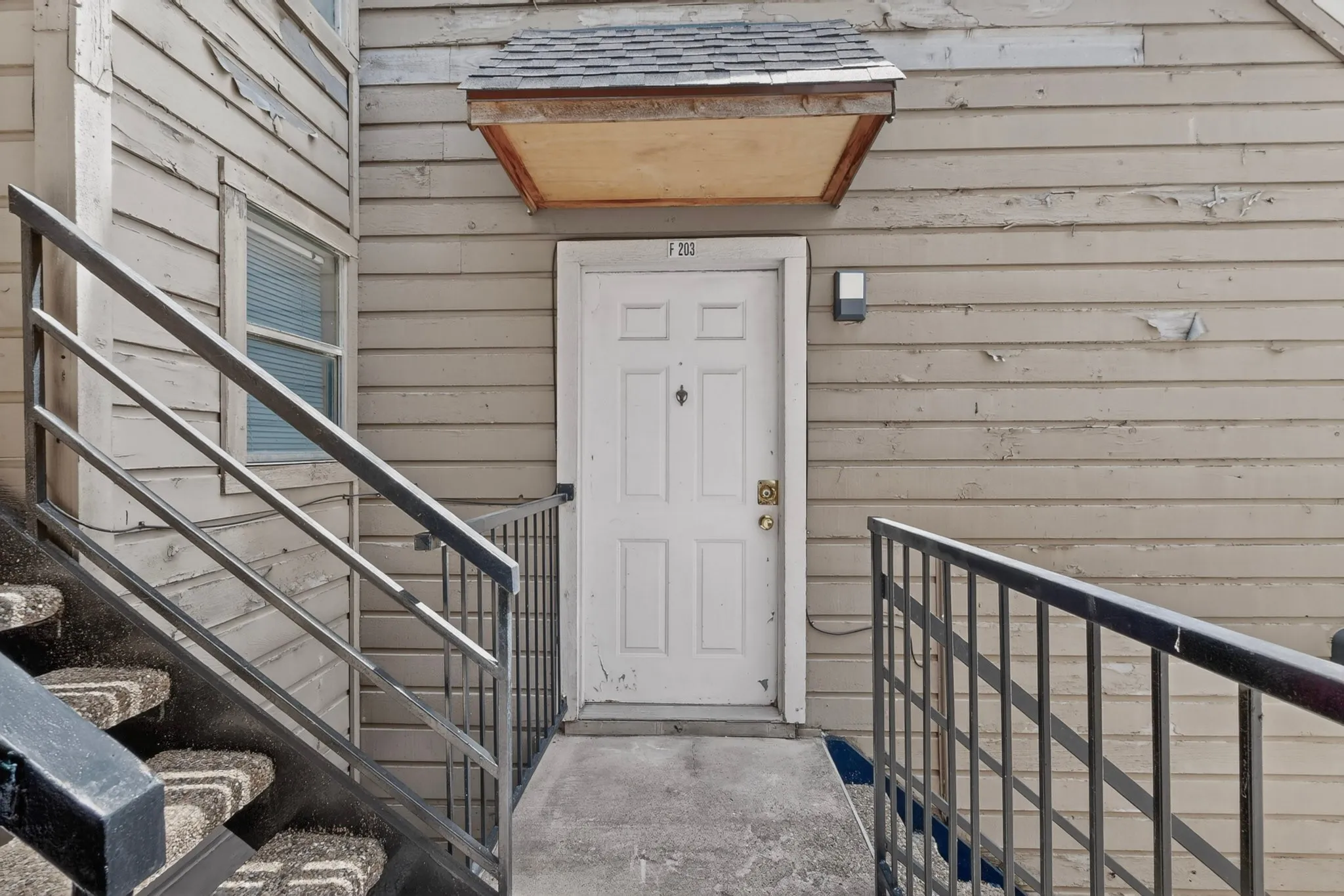 Entryway featuring a white paneled door, an overhead shingled awning, and a wall-mounted exterior light fixture