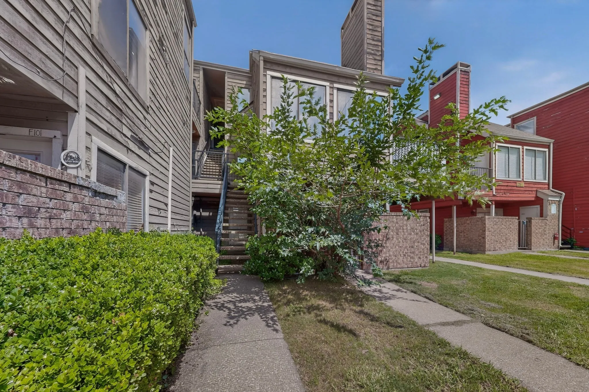 Multi-level exterior featuring wood siding, brick accents, concrete pathways, and mature shrubs