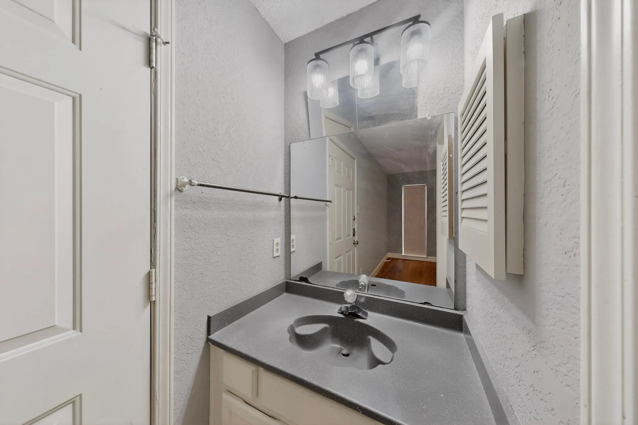 Vanity area featuring a built-in sink with a single-handle faucet, a wall-mounted mirror, and a three-light fixture