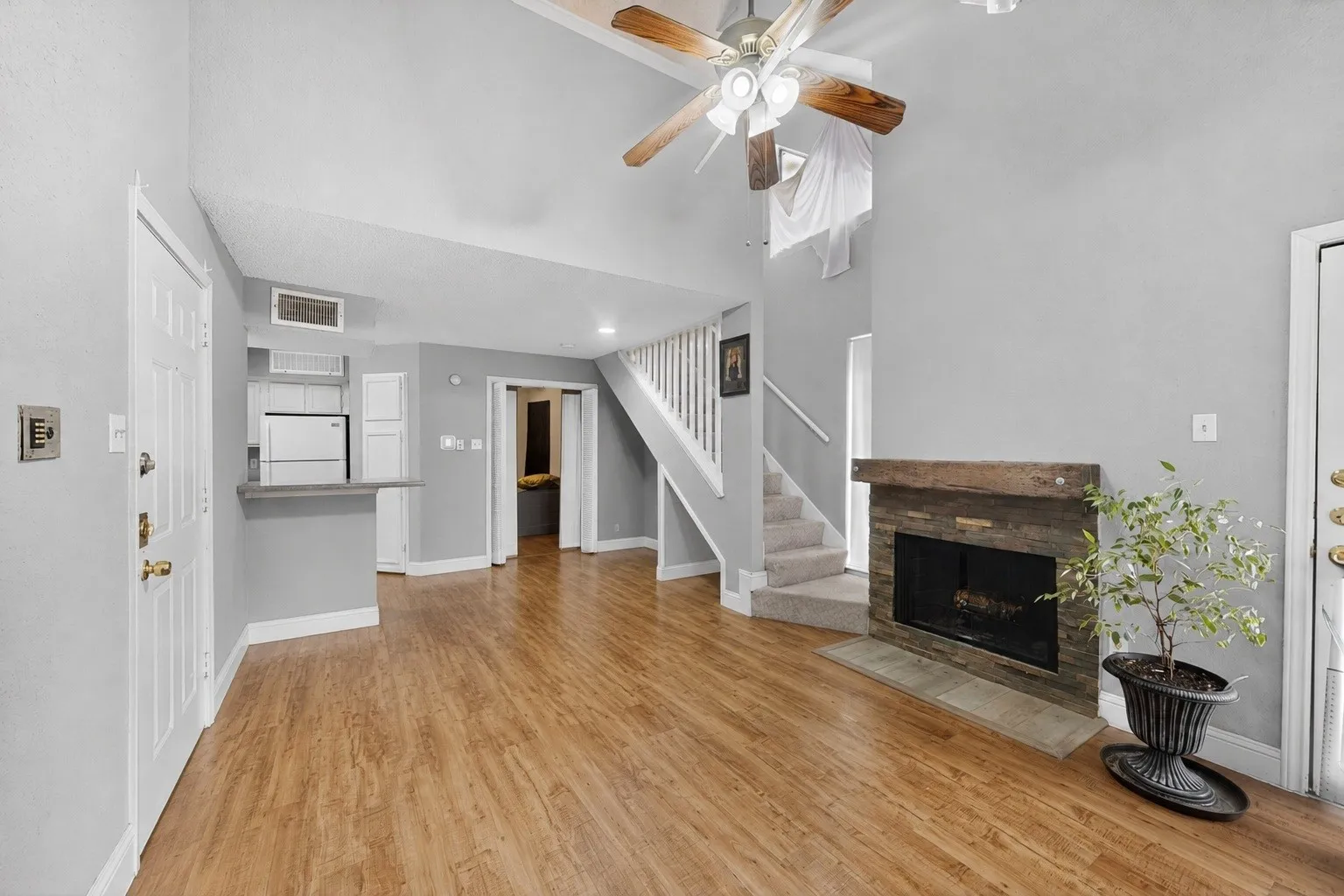 Spacious living area featuring wood-finish flooring and a stone-surround fireplace with a wood mantle