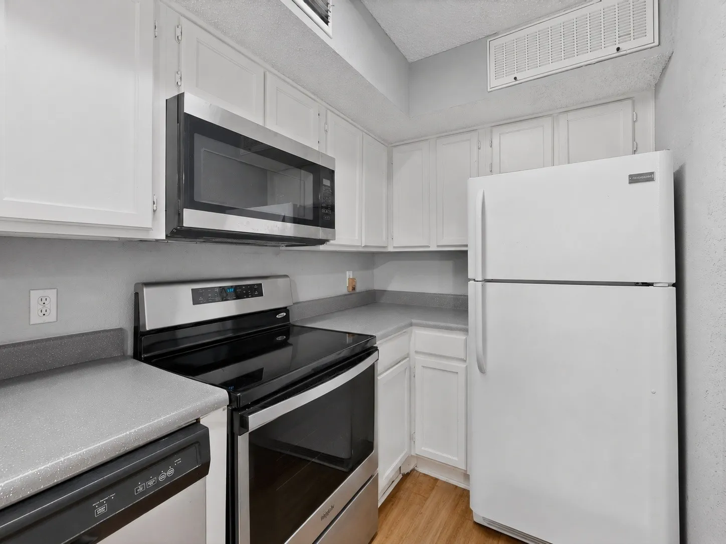 Kitchen with white cabinetry, gray countertops, stainless steel appliances, and wood-finish flooring