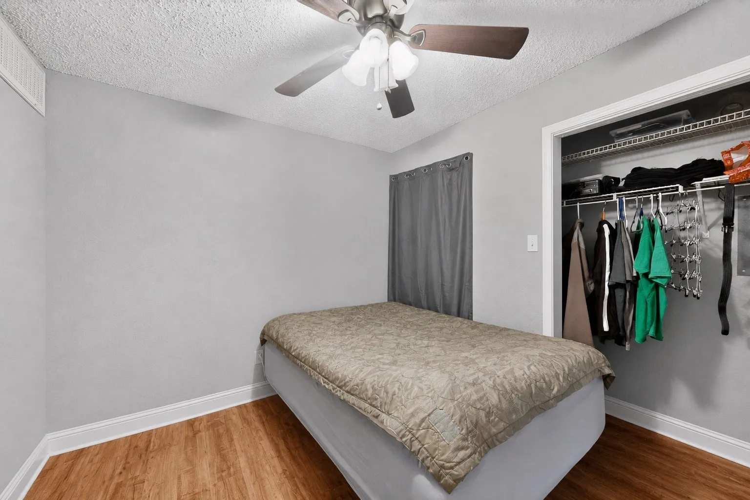 Room featuring wood-finish flooring, a ceiling fan with integrated lighting, and a closet with built-in shelving and hanging rods