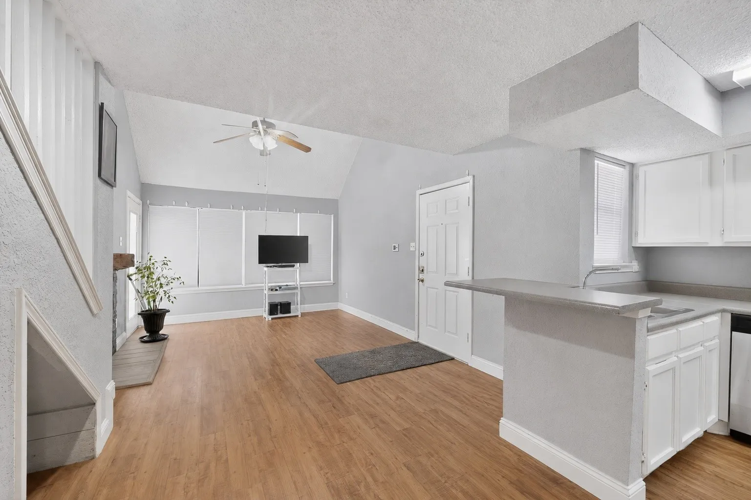 Open-concept living area featuring wood-finish flooring, vaulted ceiling with a ceiling fan, and white walls
