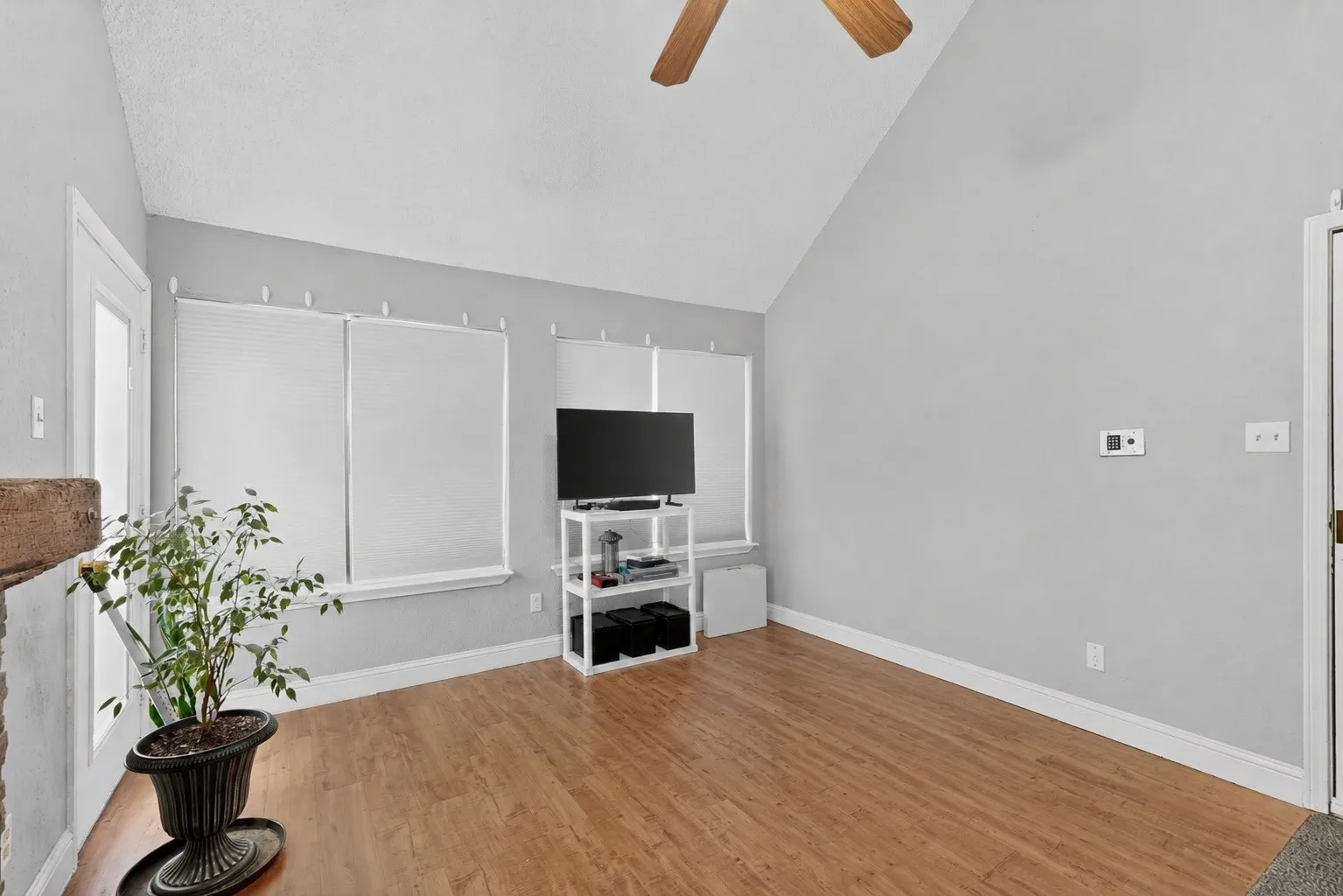 Vaulted ceilings enhance this space featuring wood-finish flooring, multiple windows with blinds, a white baseboard trim, and a ceiling fan