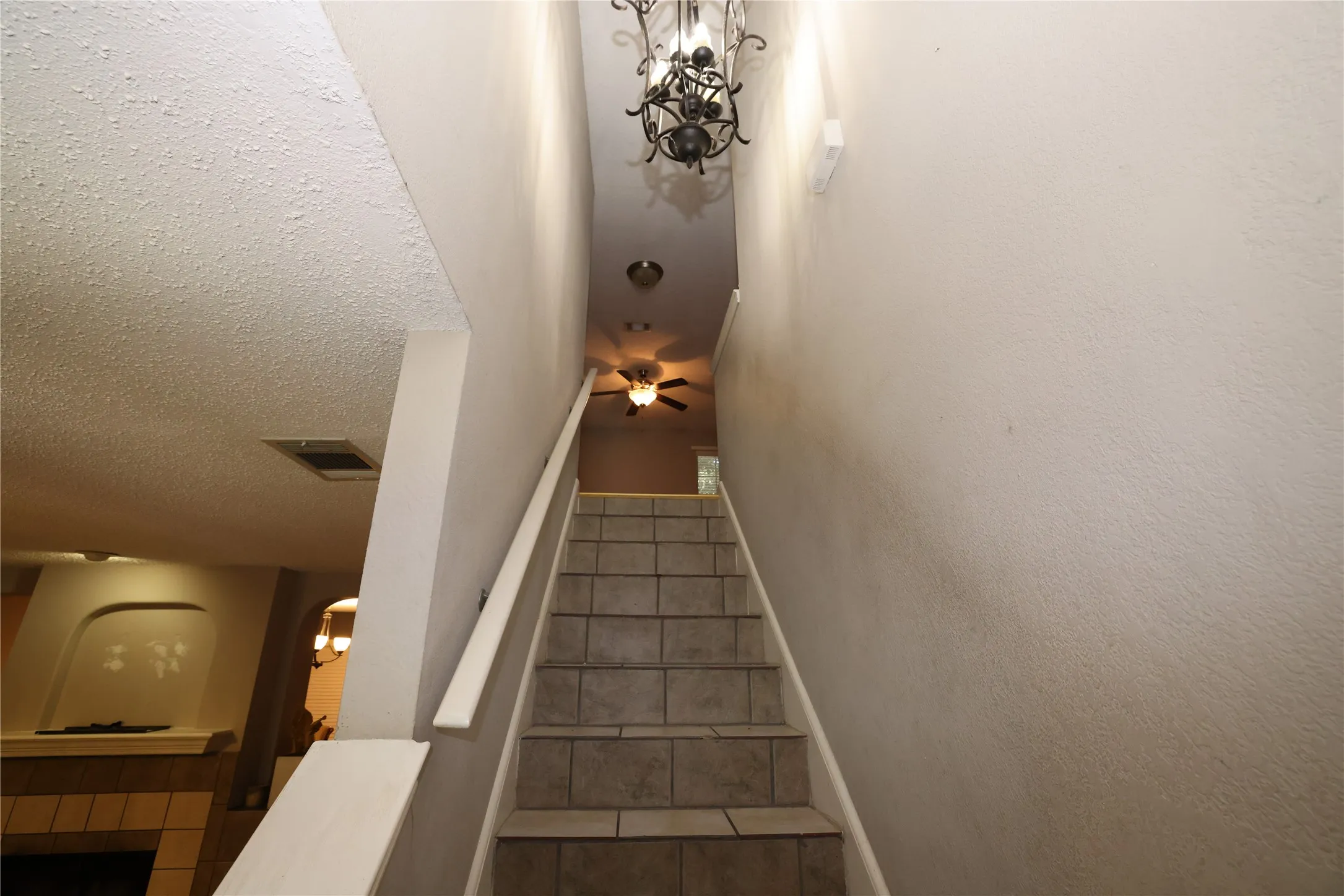 Tiled staircase with white railing, featuring a decorative chandelier and a ceiling fan at the landing