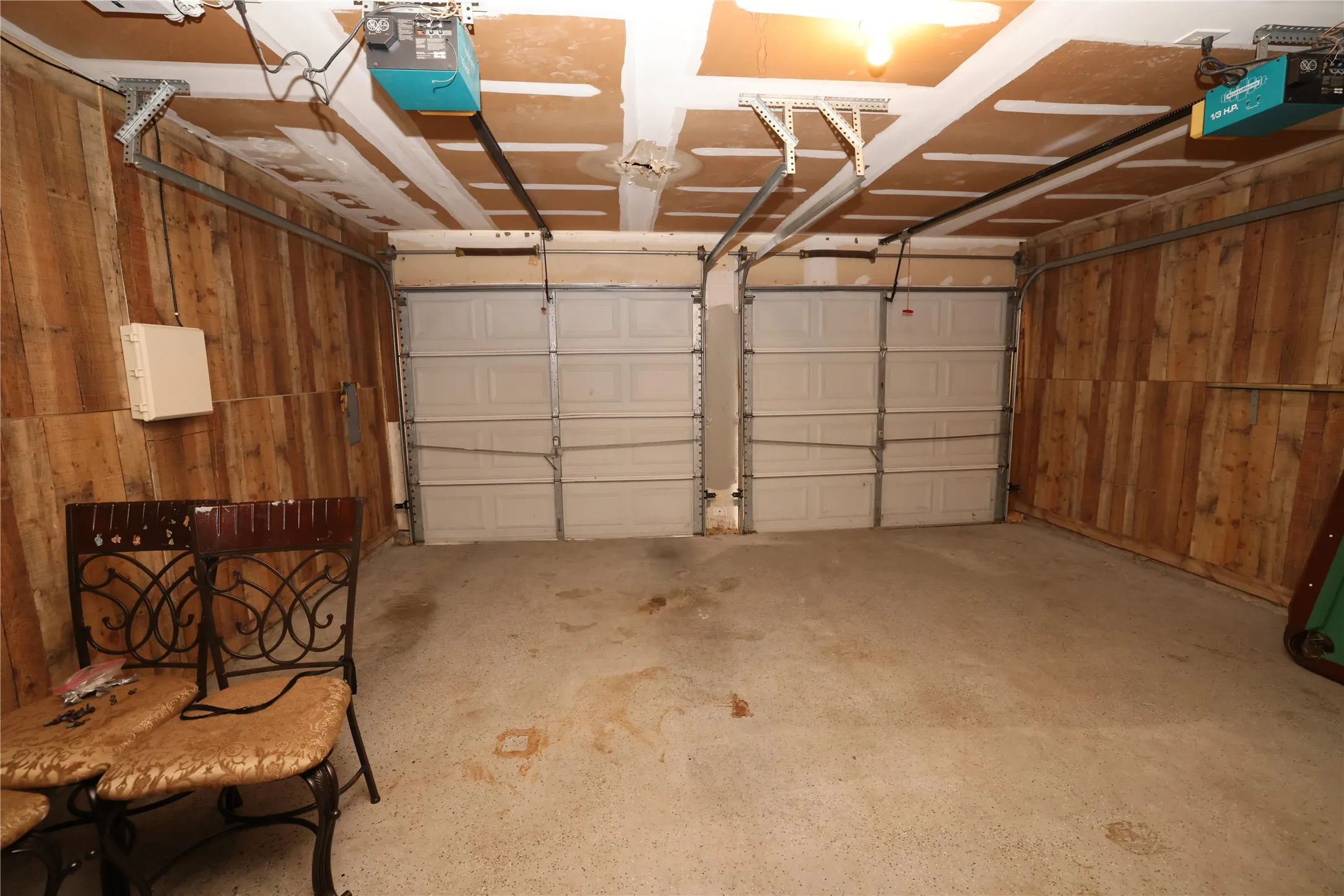 Two-car garage featuring paneled doors, exposed ceiling joists, and wood-paneled walls