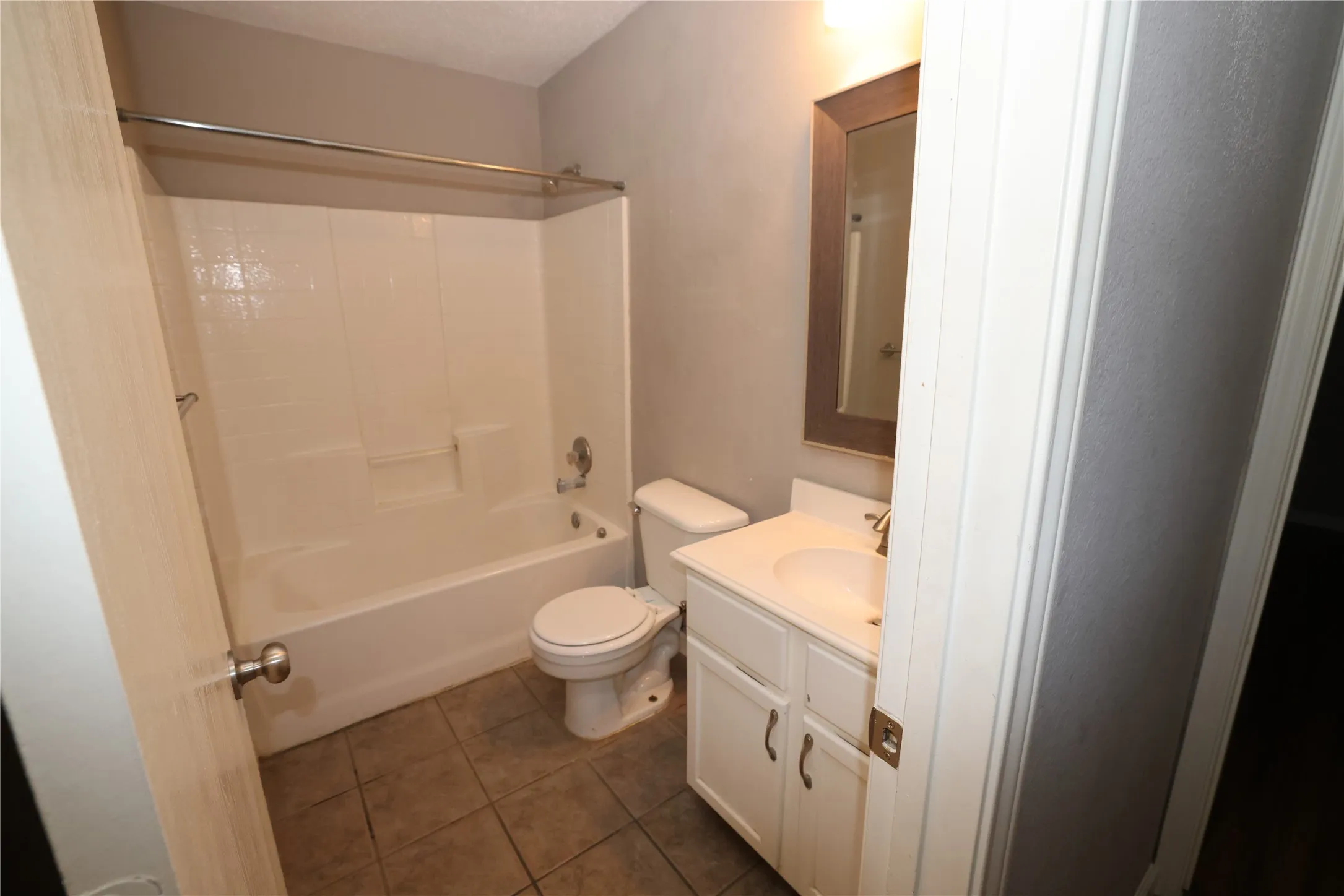 Bathroom featuring a white vanity with cabinet storage, a framed mirror, and a white tub with shower surround