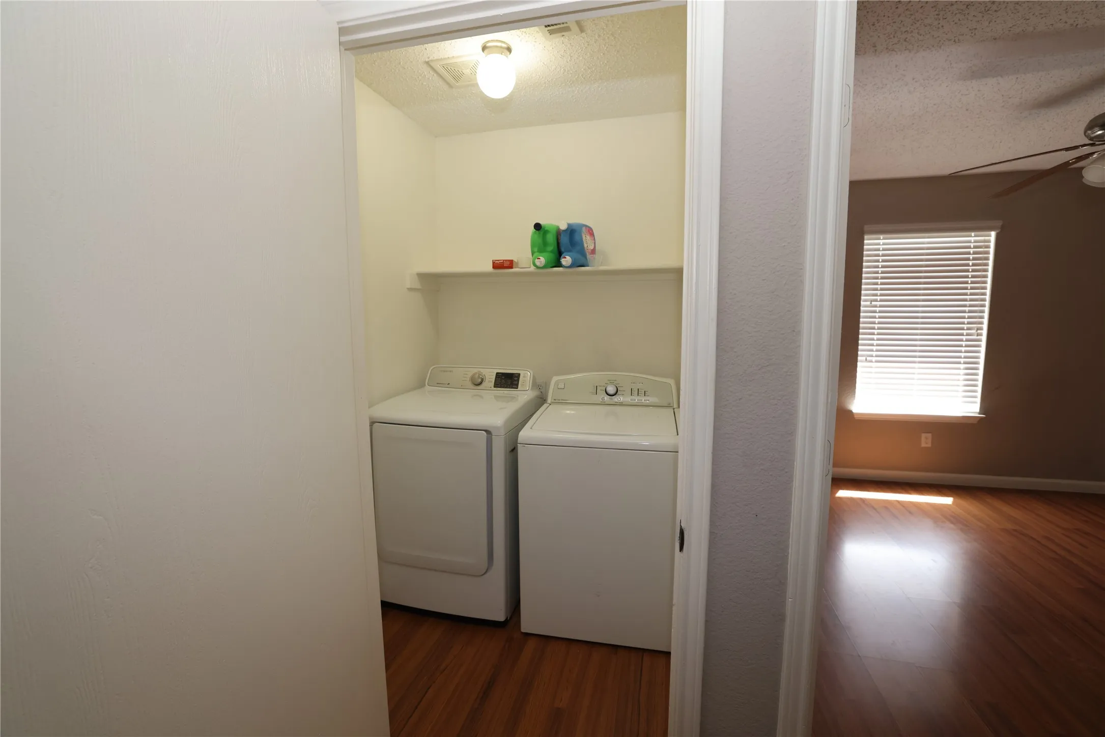 Laundry closet with a built-in shelf, overhead lighting, and wood-finish flooring