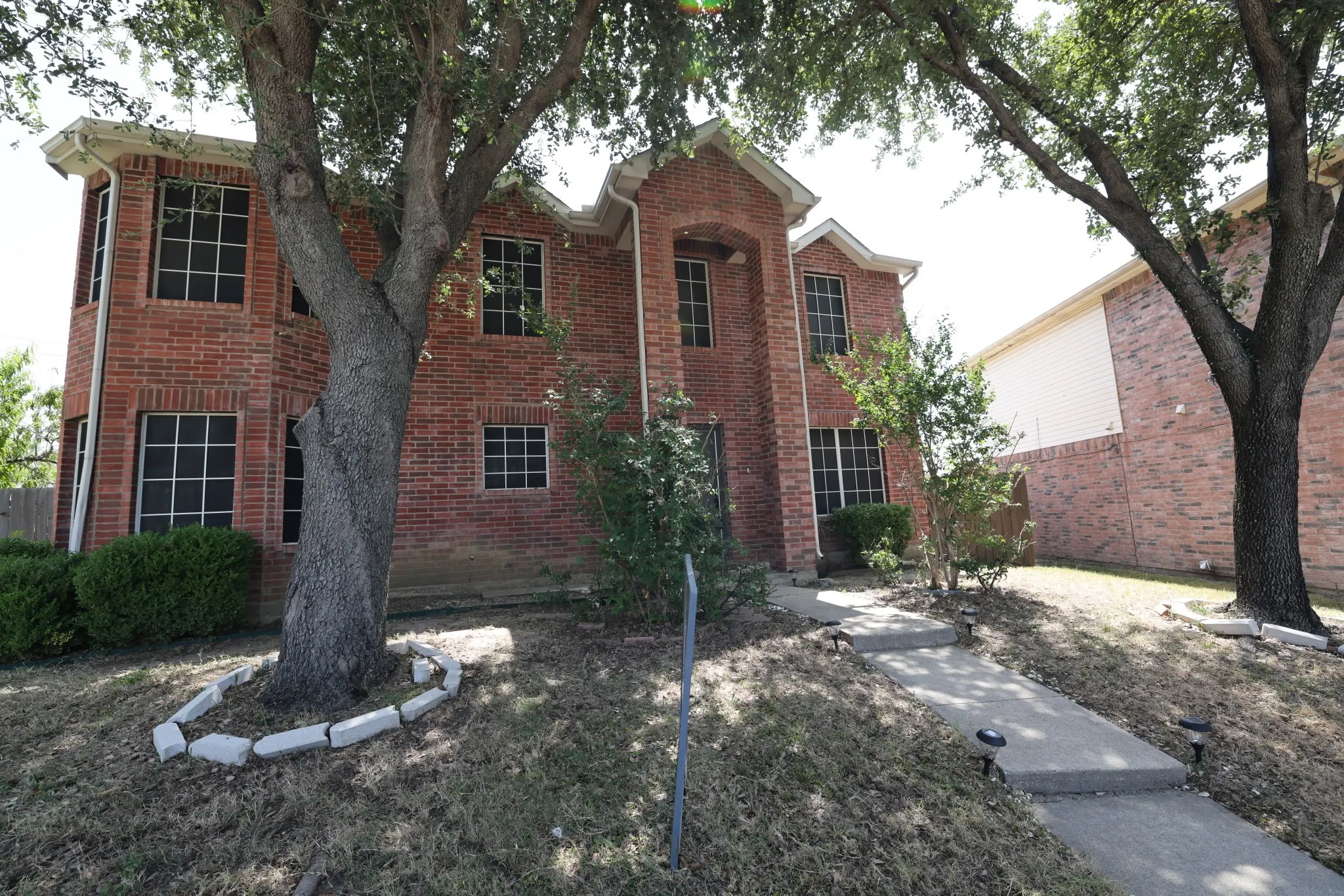Two-story brick exterior featuring a prominent arched entry, multiple windows with grid patterns, and a concrete walkway