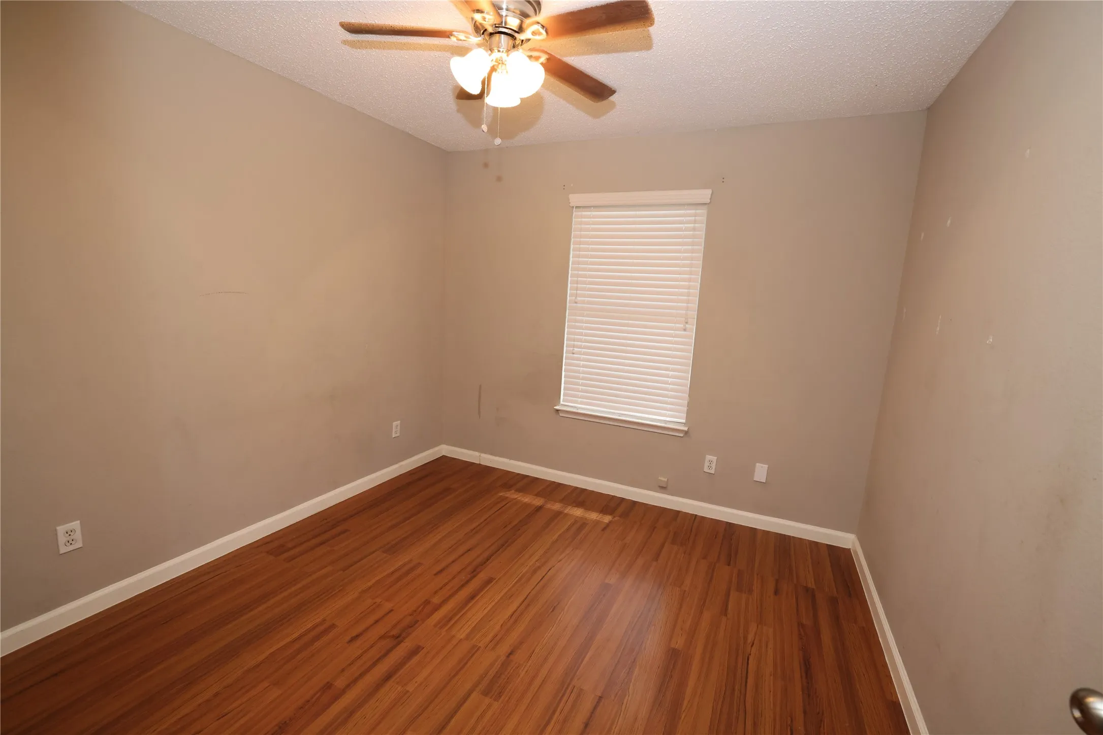 Room featuring wood-finish flooring, neutral wall tones, a window with blinds, and a ceiling fan with integrated lighting