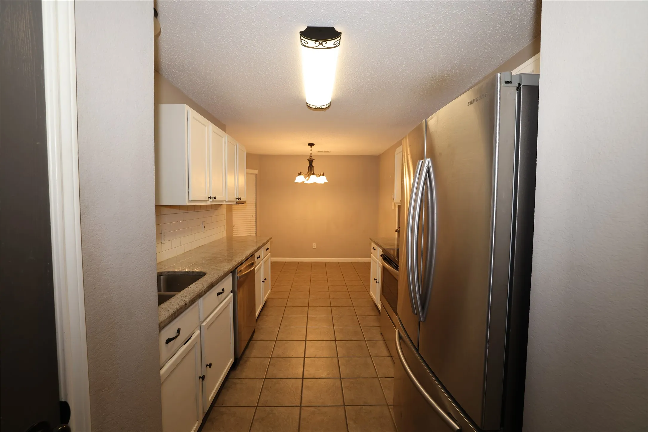 Galley kitchen featuring white cabinetry, a double basin sink, stainless steel appliances, granite countertops, and tile flooring