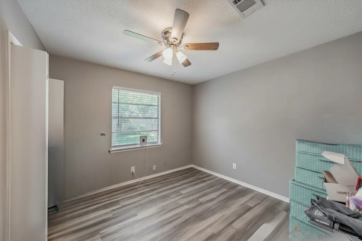Secondary bedroom featuring vinyl wood look floor and a ceiling fan. Photo has been digitally enhanced.