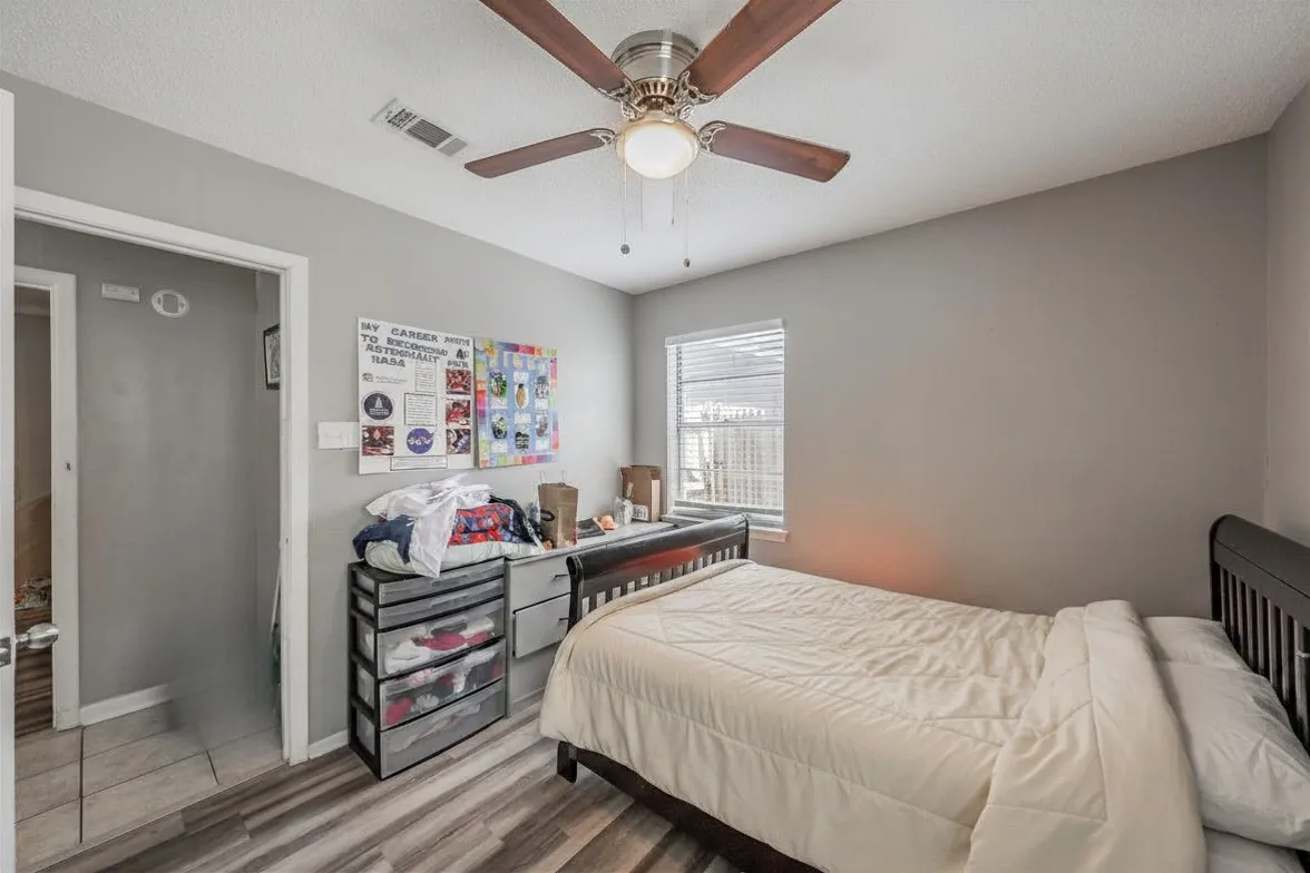 Secondary bedroom featuring vinyl wood look floor and a ceiling fan. Photo has been digitally enhanced.