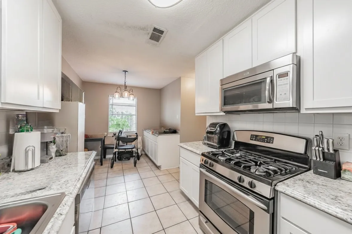 Galley style kitchen featuring white shaker cabinets, stainless steel appliances, and tile flooring. Photo has been digitally enhanced.